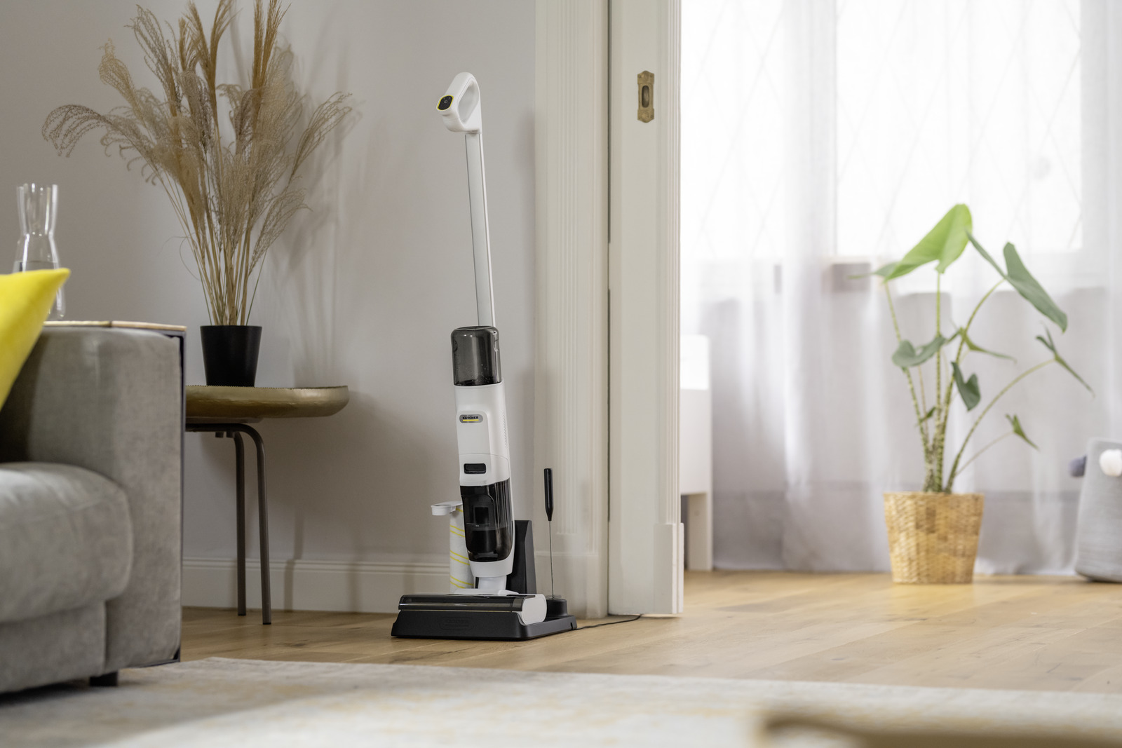 Biały odkurzacz do podłóg ładuje się obok drzwi w salonie.