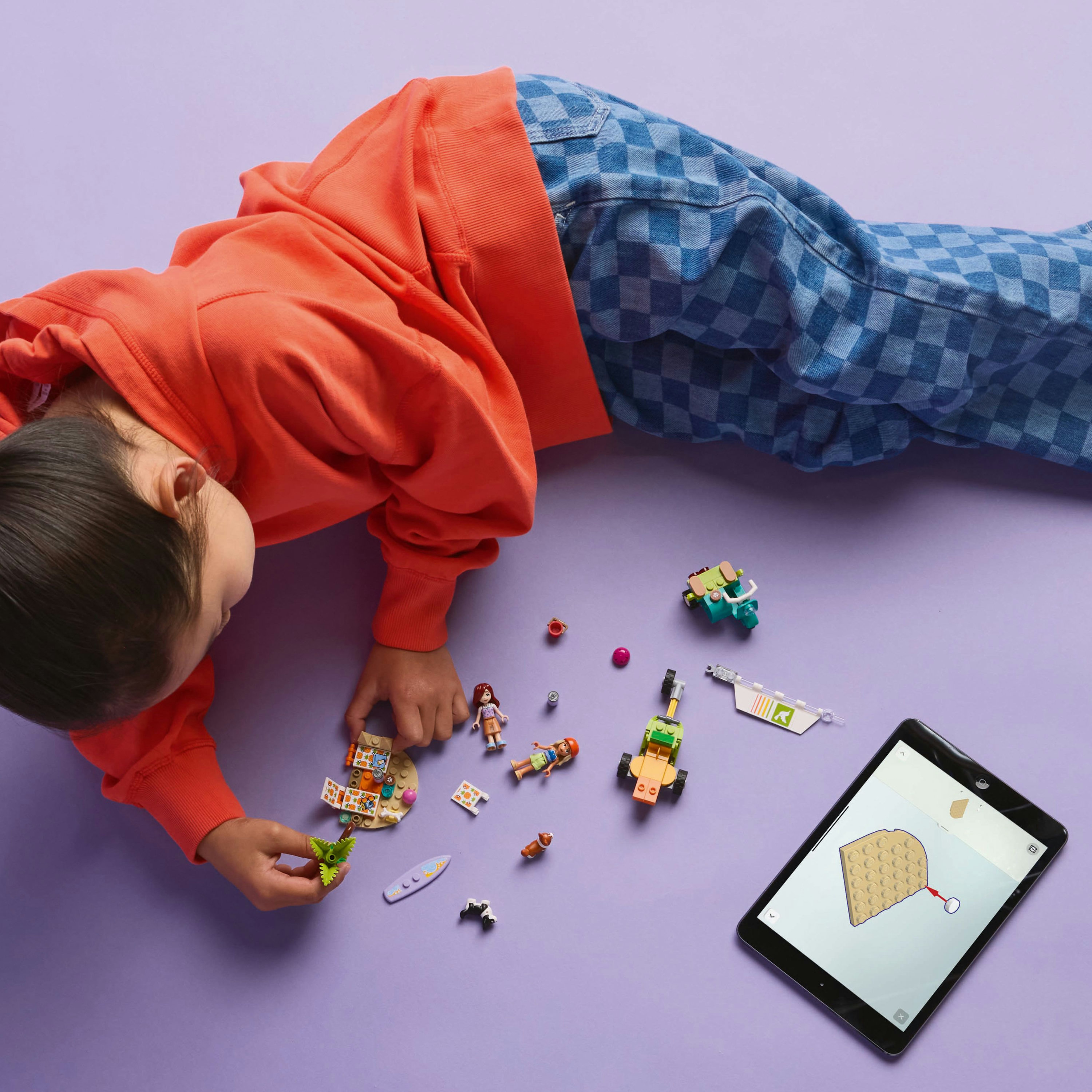 Dziecko bawi się zestawem Lego Friends na fioletowej powierzchni z tabletem wyświetlającym instrukcje.