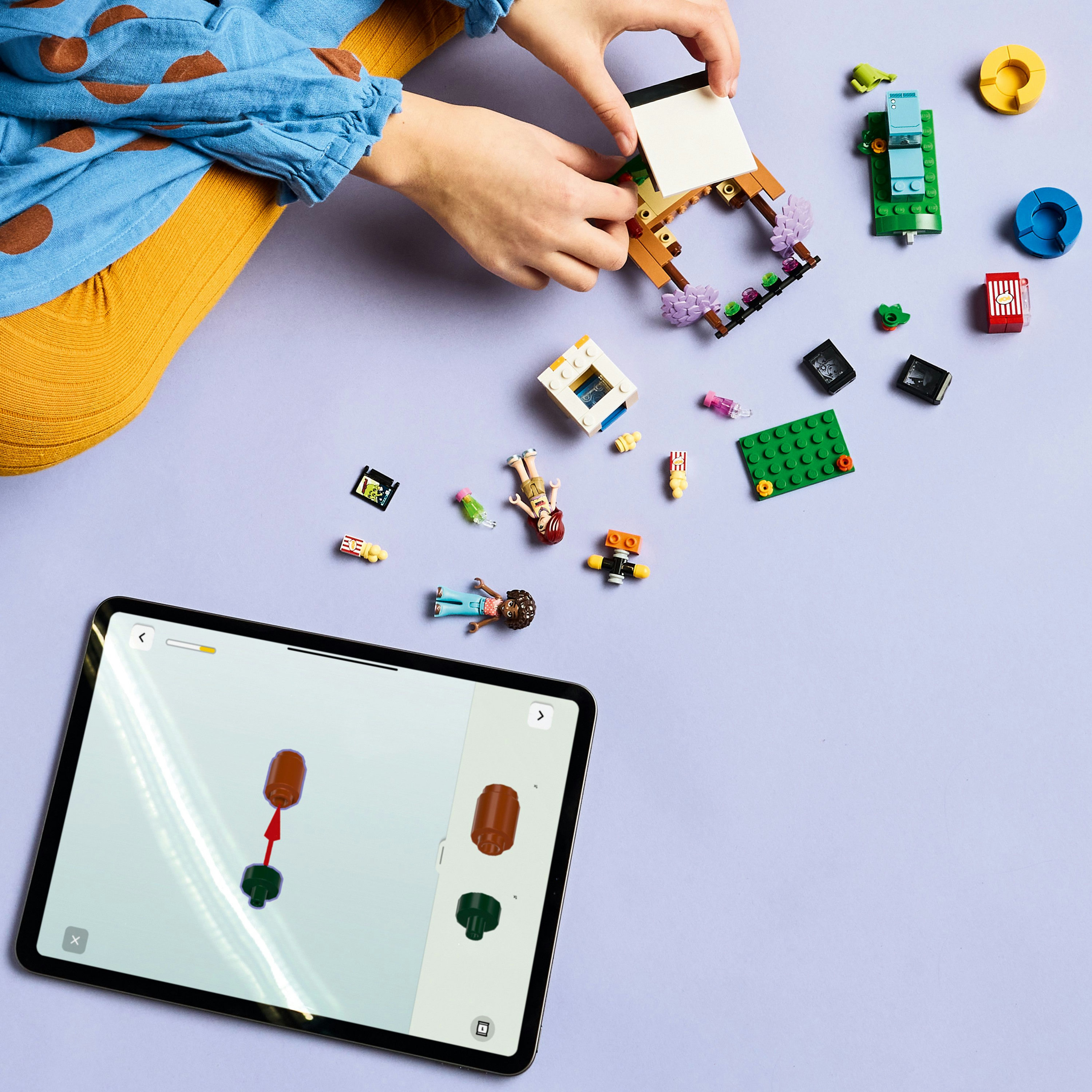 Dziecko buduje zestaw Lego Friends z motywem filmowym i tabletem pokazującym instrukcje budowania na fioletowym tle.