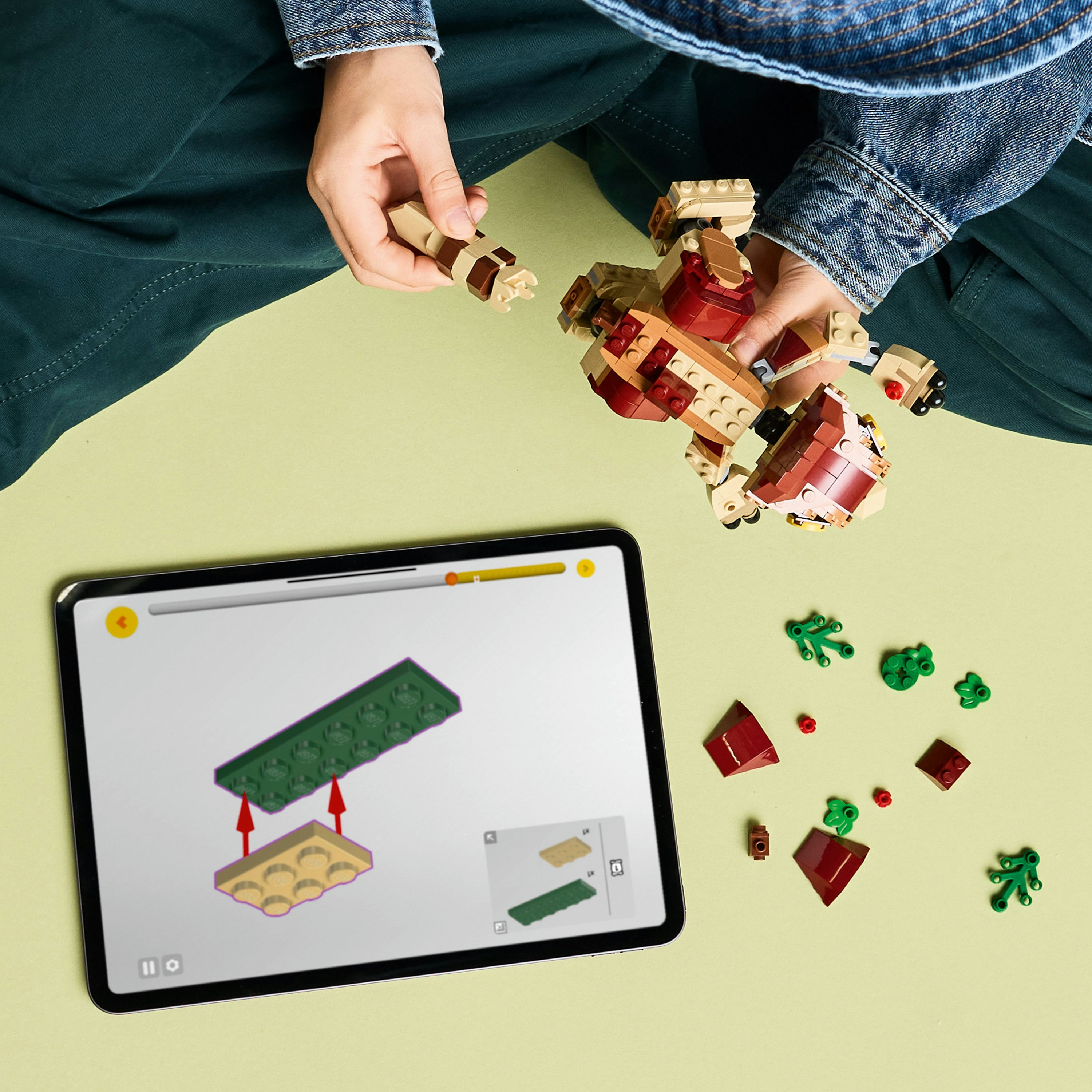 Manos construyendo Lego Aquilops con una tableta que muestra instrucciones sobre una superficie verde claro.