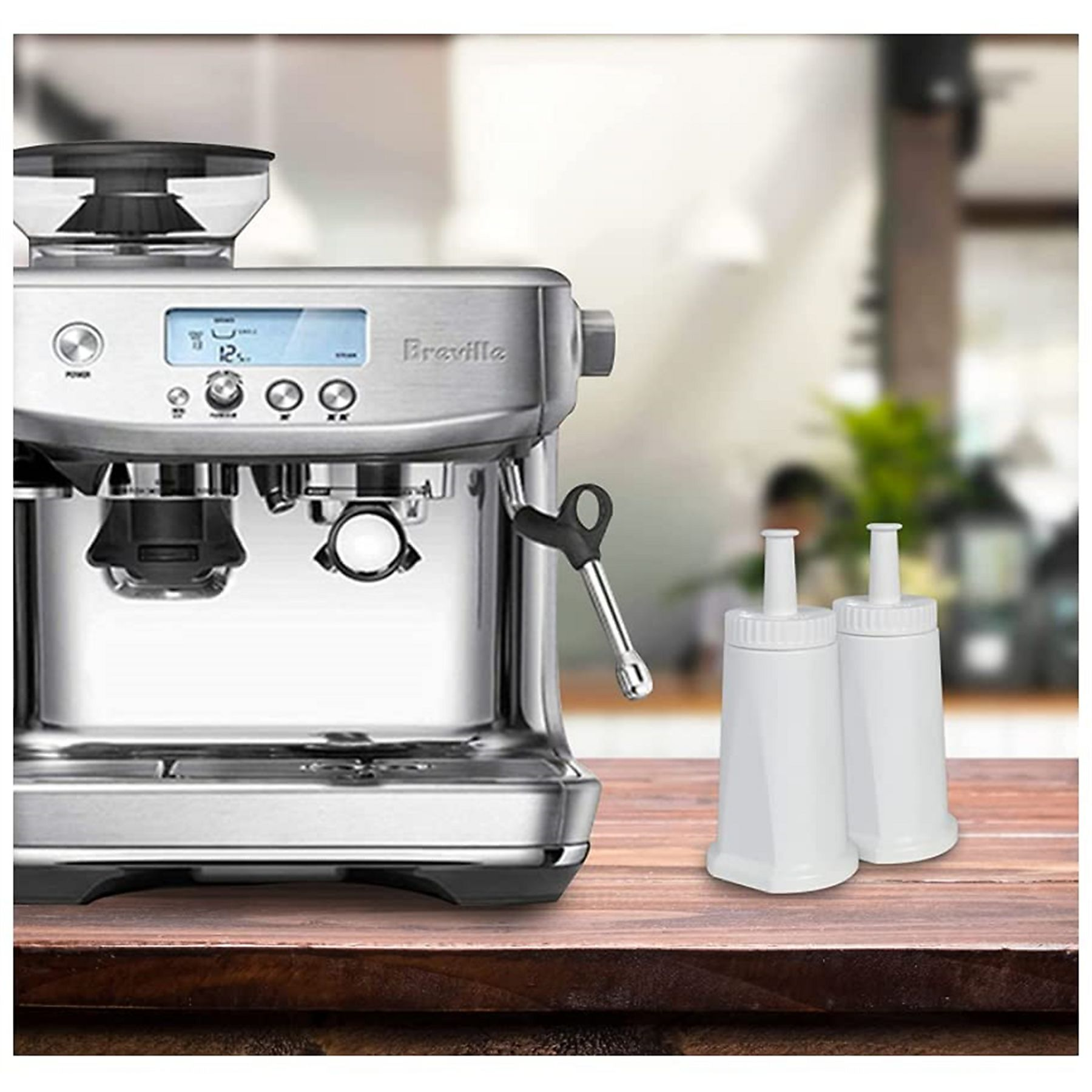 Eine silberne Espressomaschine steht auf einem Holztisch mit zwei weißen Wasserfiltern. Der Hintergrund ist verschwommen.
