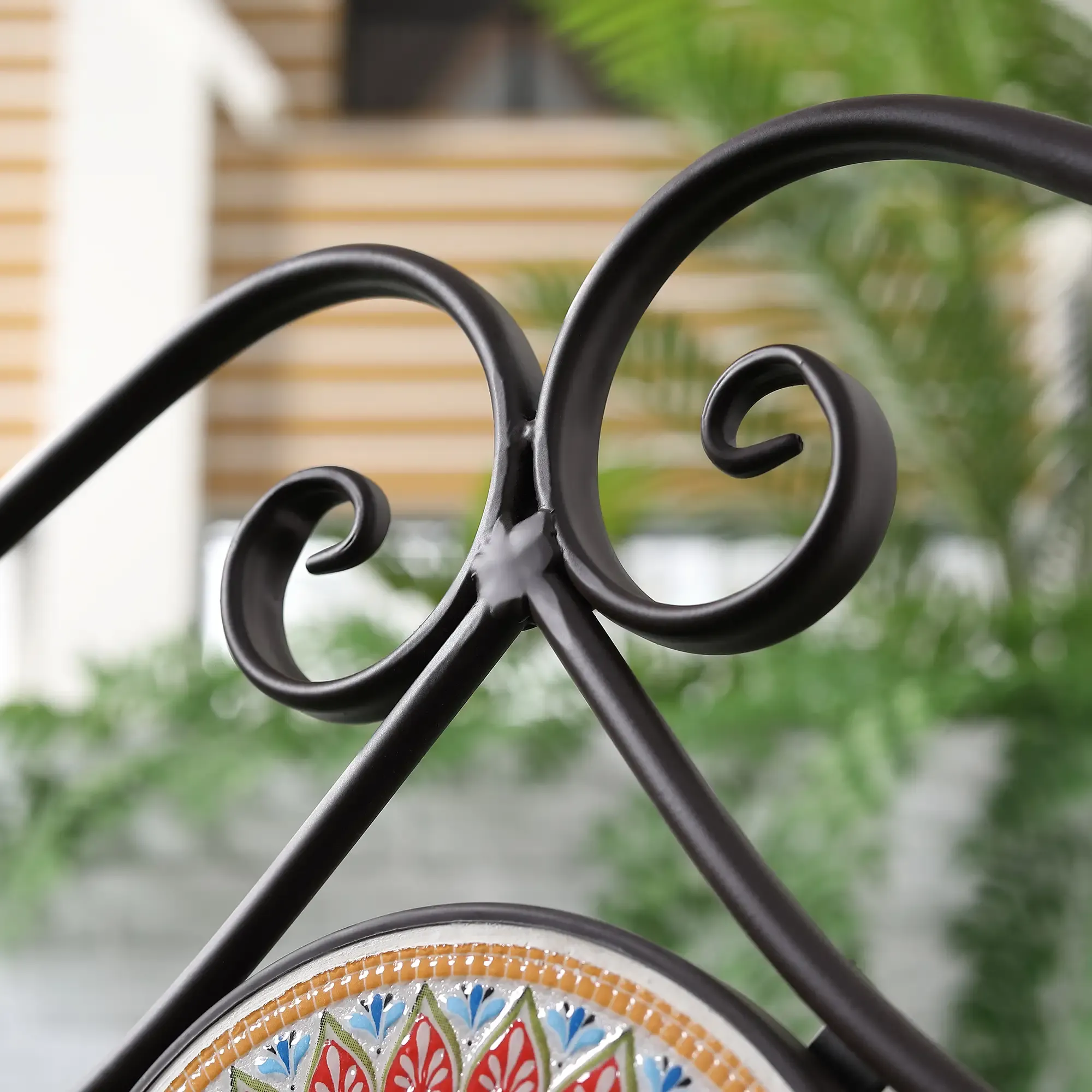 Eine Nahaufnahme zeigt die dekorative Rückseite einer braunen Metall-Gartenbank mit einem Mosaikfliesendesign.