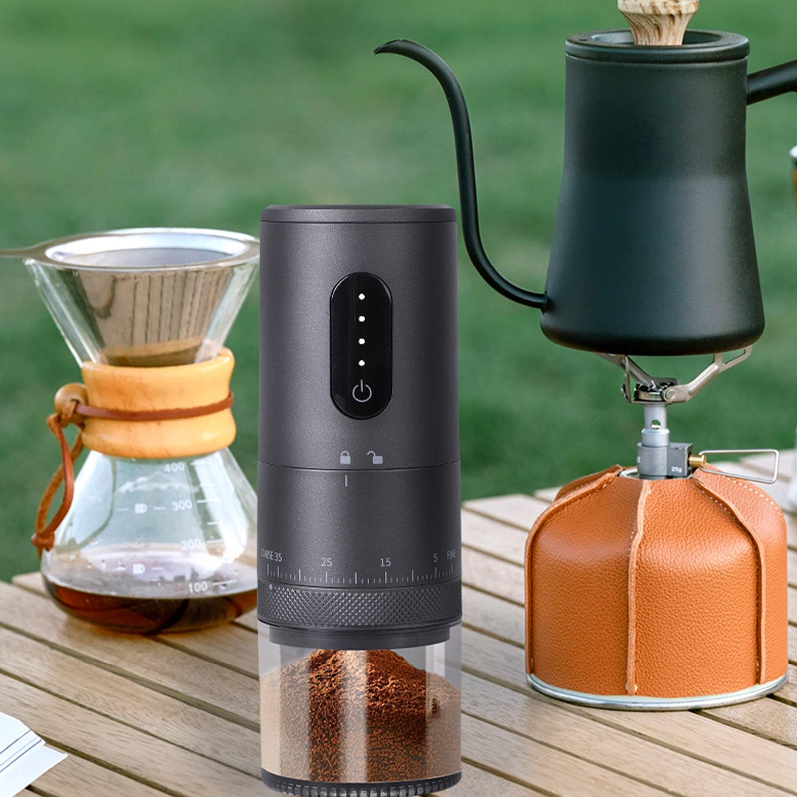 Eine Kaffeemühle auf einem Tisch mit einem Schwanenhalskessel und einer Kaffeemaschine. Die Mühle hat einen durchsichtigen Boden.