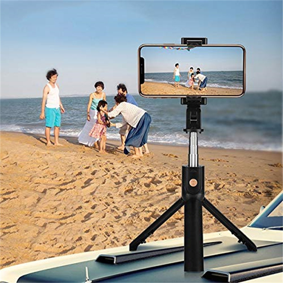 Ein Telefon auf einem Stativ filmt Menschen an einem Strand, mit einer Motorhaube im Vordergrund.