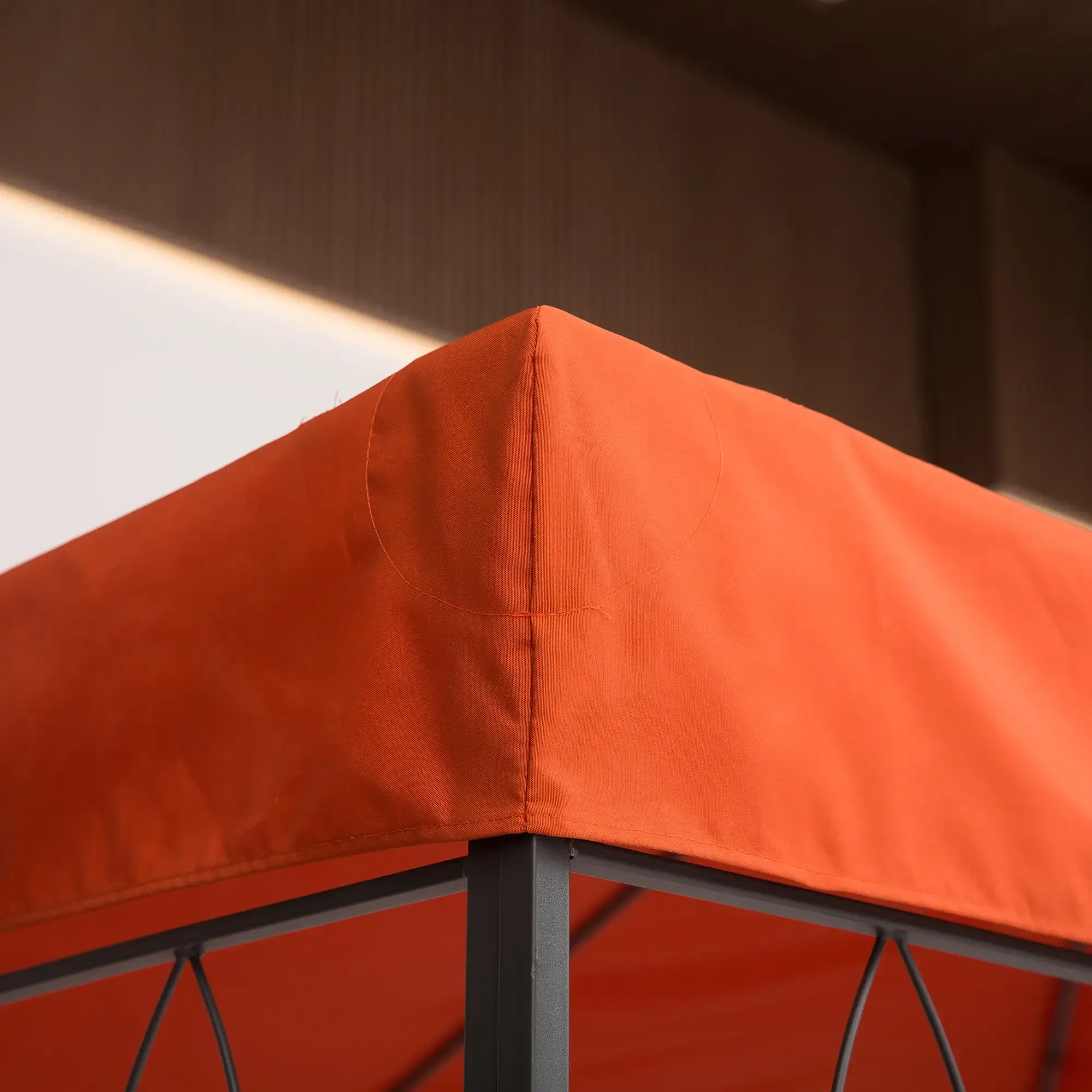 Eine Ecke eines orangefarbenen Gazebodachs mit dunklen Metallstützen vor einem neutralen Hintergrund.