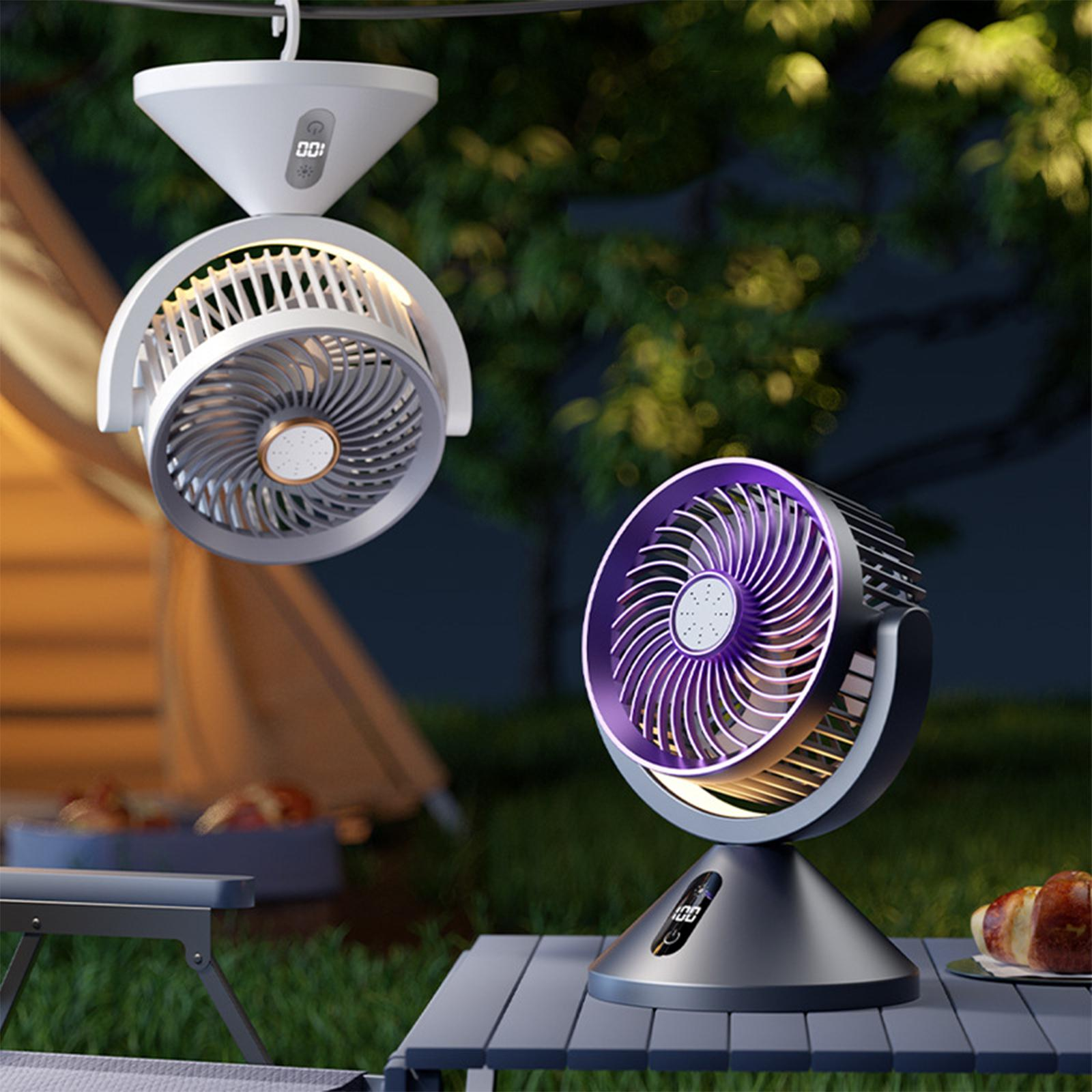 Zwei Ventilatoren, einer weiß hängend und einer lila auf einem Tisch, werden nachts in einer Campingszene gezeigt.