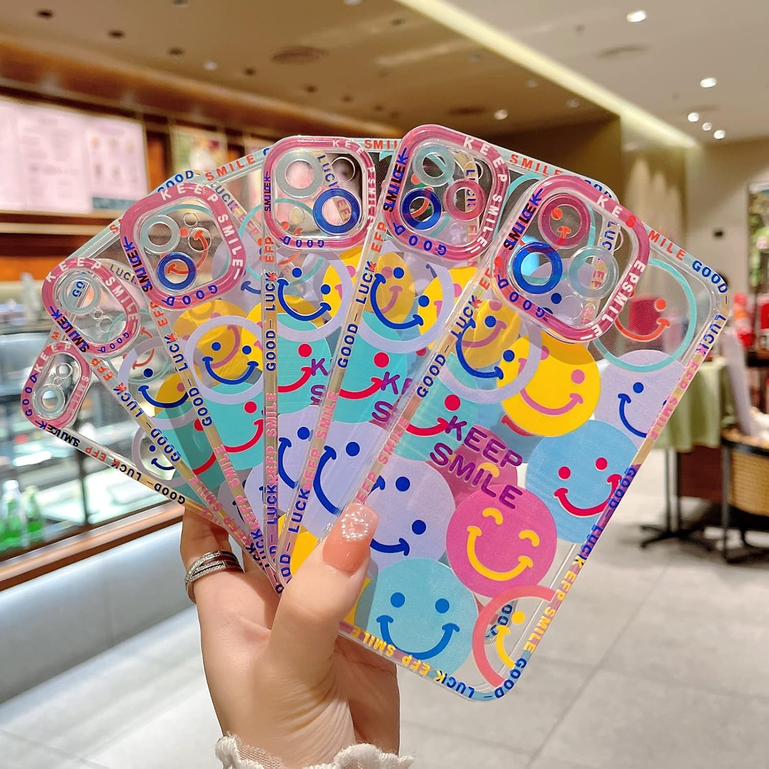 Eine Hand hält mehrere durchsichtige Handyhüllen mit bunten Smileys und den Worten 'Keep Smile' und 'Luck EFP Smile'.