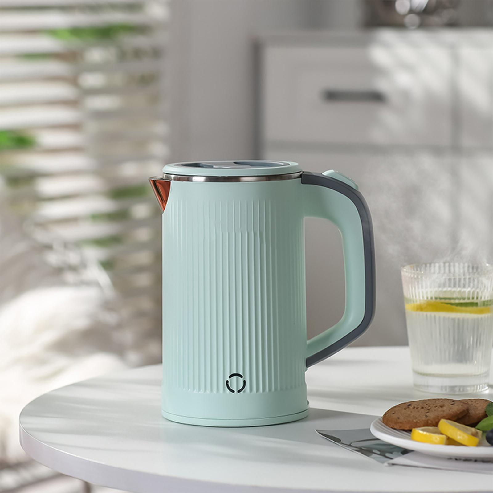 Ein mintgrüner elektrischer Wasserkocher mit einem grauen Griff steht auf einem weißen Tisch neben einem Glas Wasser.