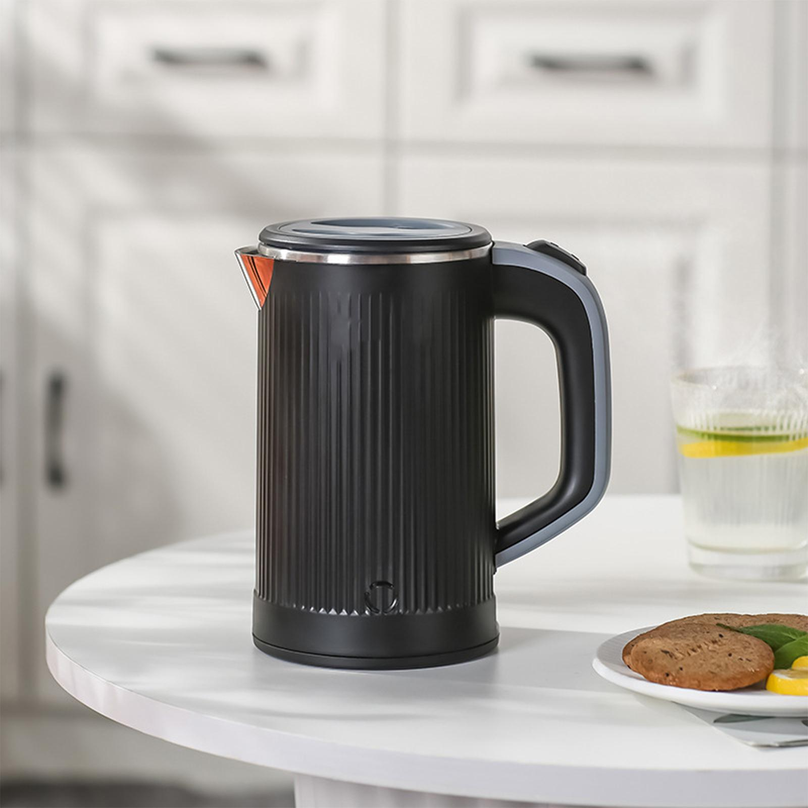 Ein schwarzer elektrischer Wasserkocher mit grauem Griff auf einem weißen Tisch, neben einem Glas Wasser.