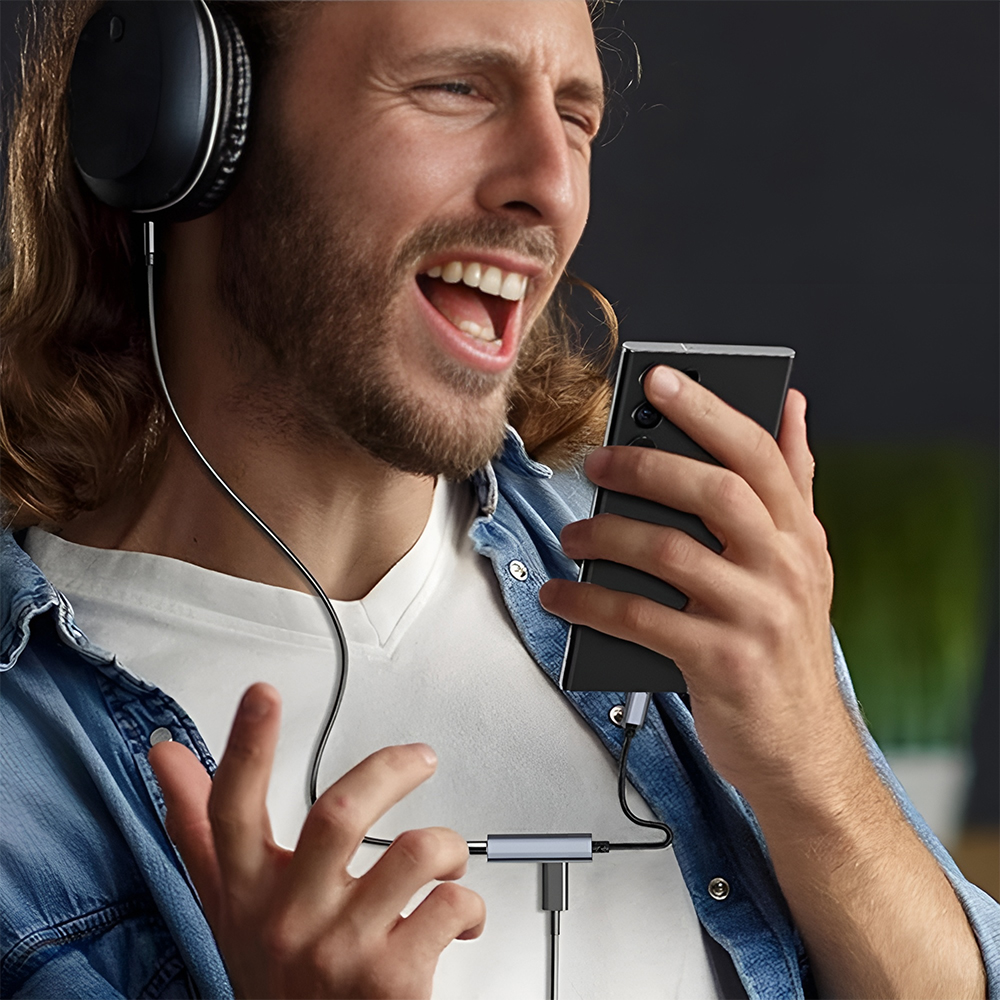 Eine Person hört Musik auf einem Telefon mit Kopfhörern, die über einen Adapter verbunden sind.