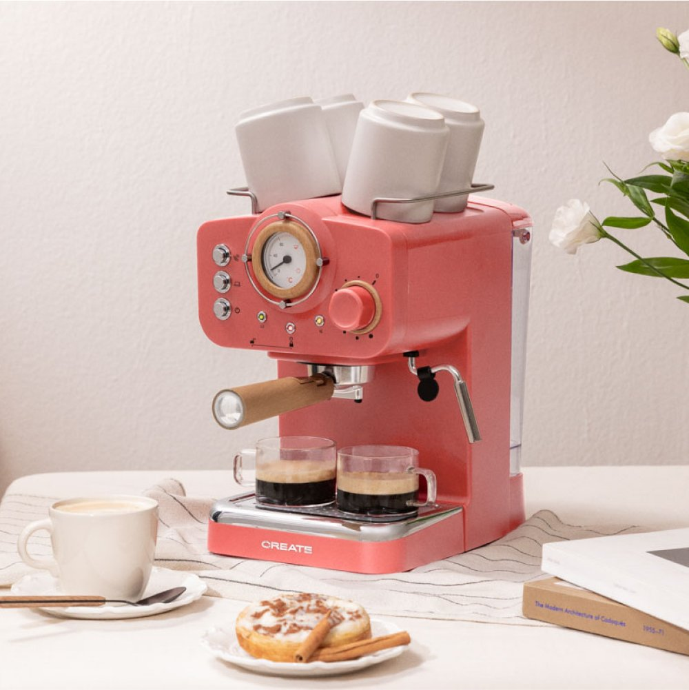 Una máquina de café espresso rosa con tazas, café y un donut en una mesa.