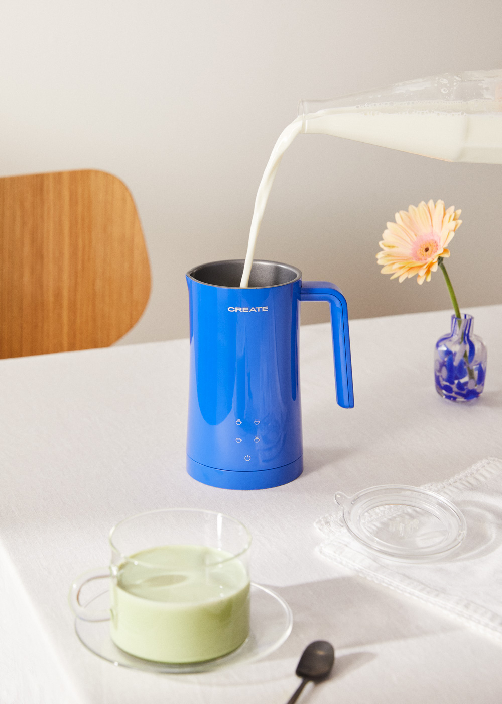 Se vierte leche en un espumador de leche azul Create junto a una bebida, una flor y una tapa.