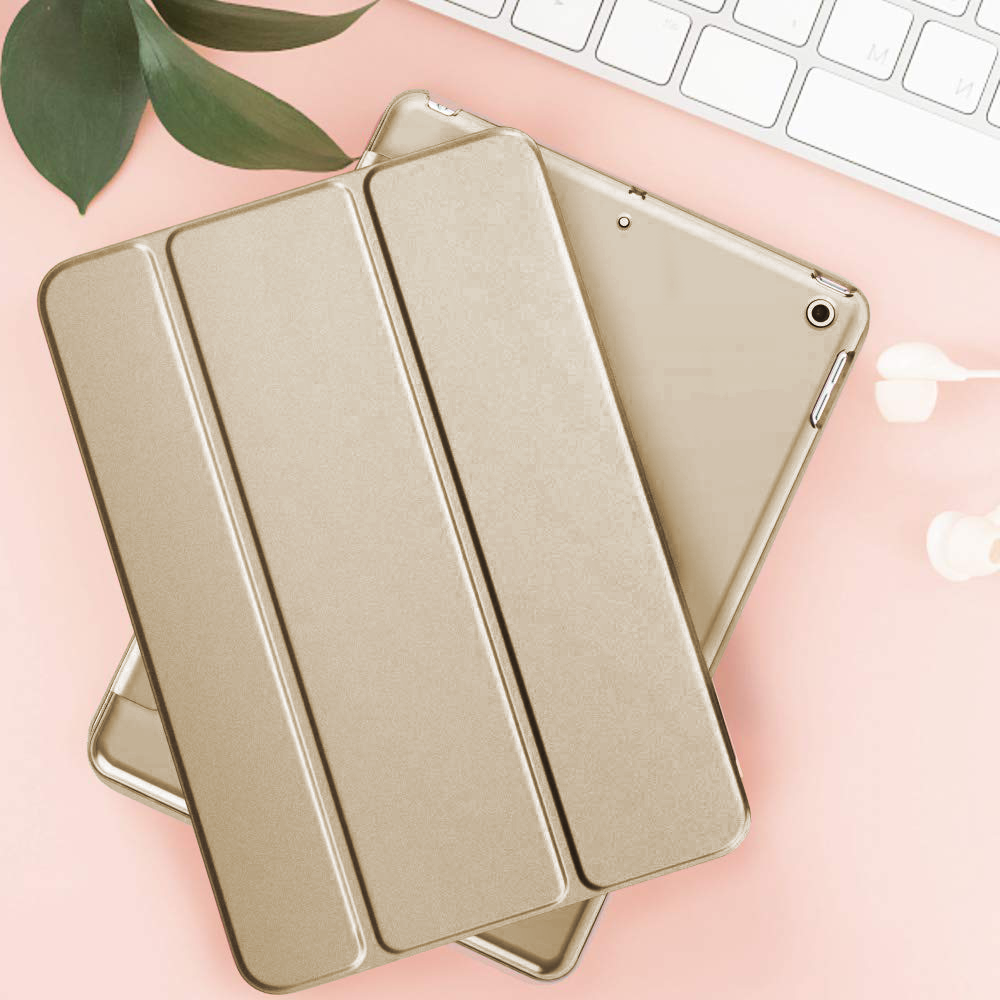 Ein rehbraunes iPad mit einer Klapphülle liegt auf einer rosafarbenen Oberfläche neben einer Tastatur und Ohrhörern.