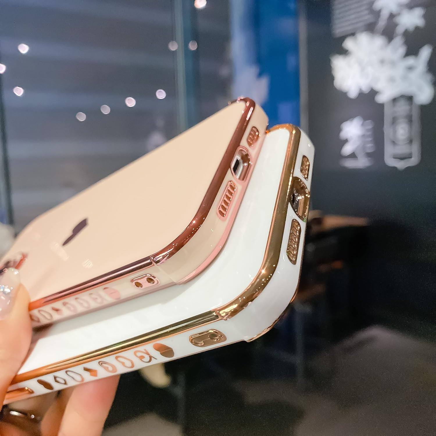 Zwei iPhones mit goldenen Verzierungen und Herzmotiven. Eines ist weiß und das andere hellrosa, in einer Hand gehalten.