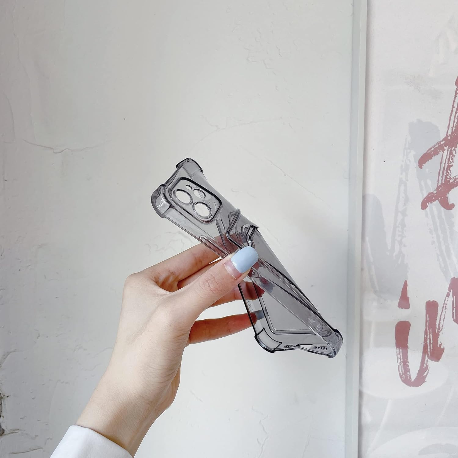 Hand, die eine durchscheinende graue Handyhülle vor einer weißen Wand mit Graffiti hält.
