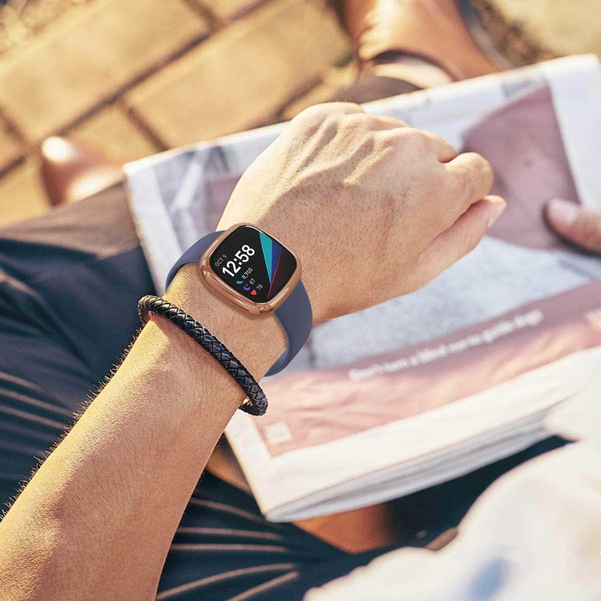 Person, die eine Smartwatch mit marineblauem Armband und roségoldenem Gehäuse trägt und im Freien eine Zeitung liest.
