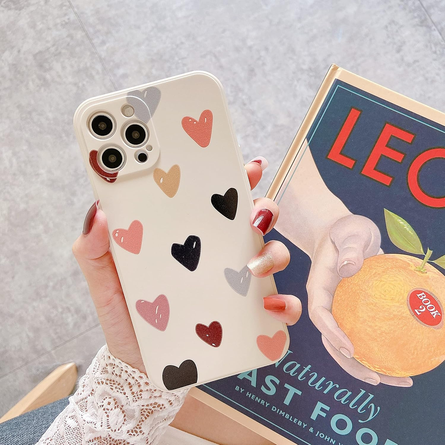 Eine Hand hält eine beige Handyhülle mit bunten Herzen neben einem Vintage-Buch.