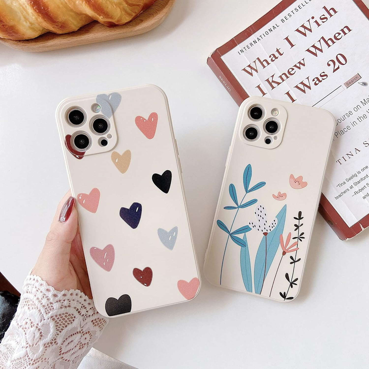 Zwei Handys mit beigen Hüllen, eines mit Herzen und eines mit floralen Mustern, auf einem Tisch.