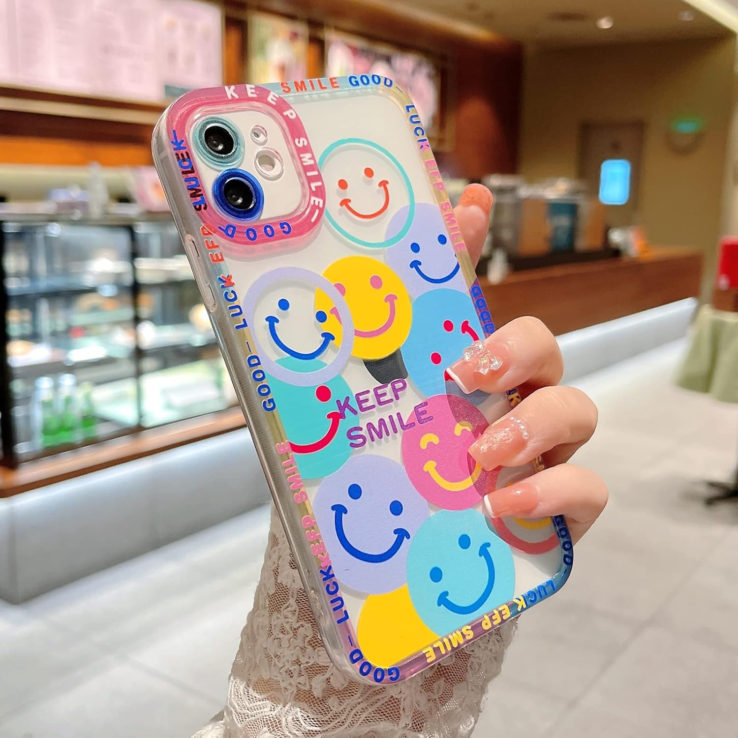Eine Handyhülle mit Smiley-Gesichtern wird in einer Hand gehalten. Die Hülle ist durchsichtig mit rosa Rand.