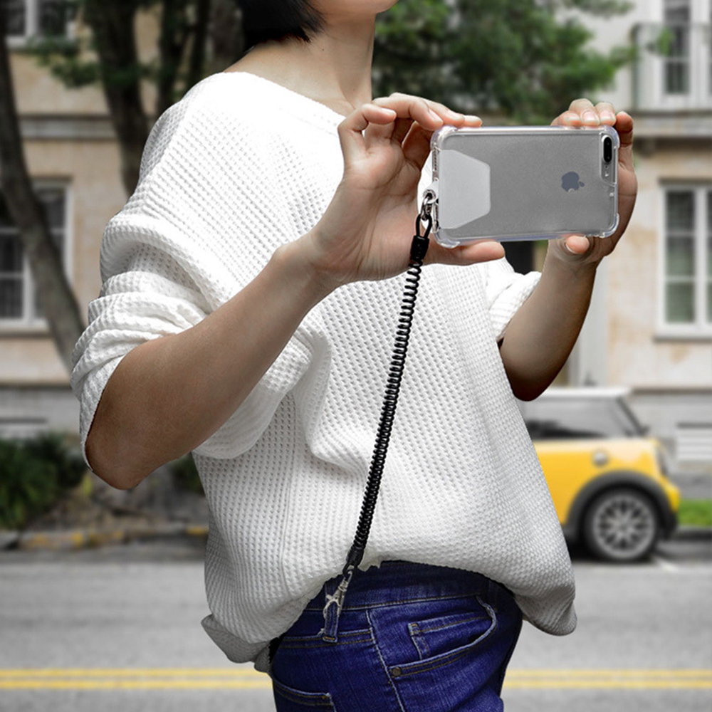 Eine Person hält ein Telefon mit einer transparenten Hülle und einem Lanyard. Im Hintergrund ein gelbes Auto.