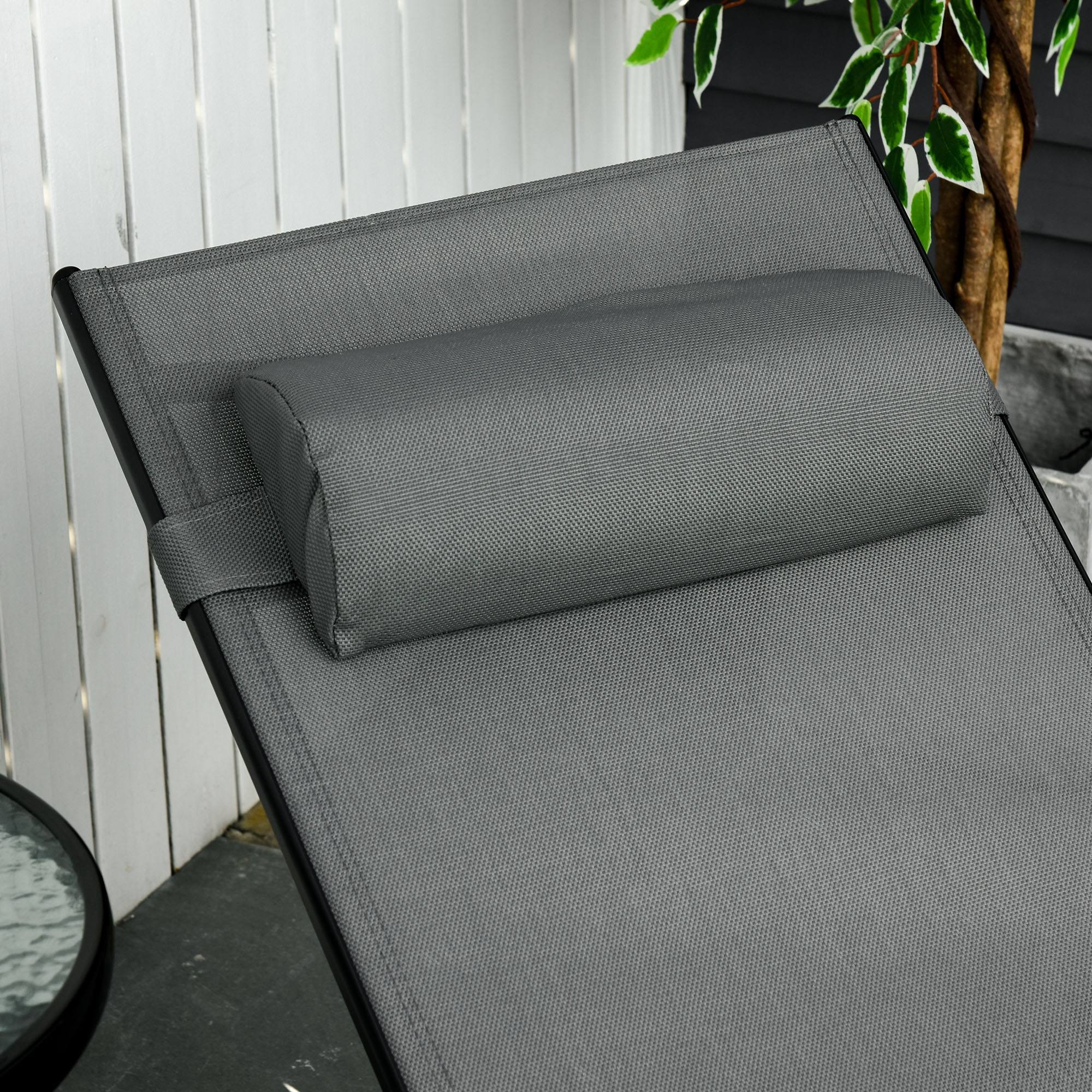 Primo piano di una chaise longue grigia con un cuscino su una terrazza in legno, accanto a un tavolino rotondo.