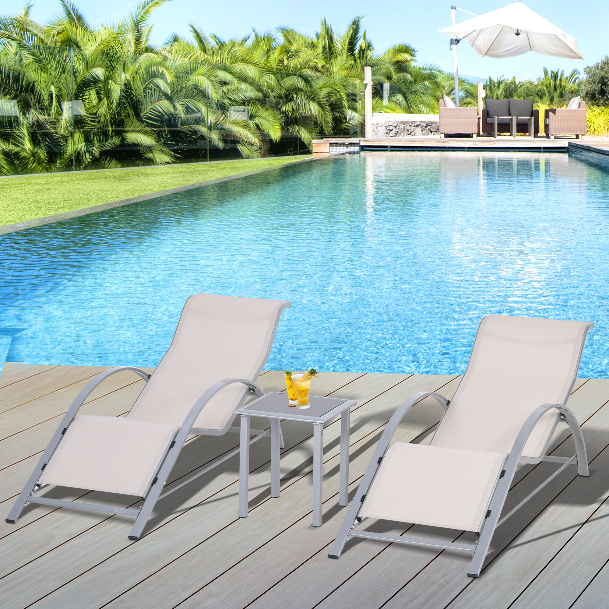 Dos tumbonas y una mesa pequeña junto a una piscina, con palmeras y una sombrilla blanca.
