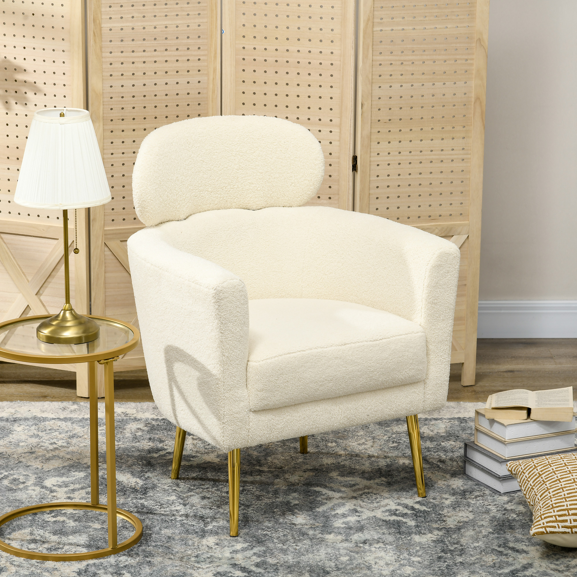 Sillón crema con patas doradas, textura suave, lámpara, mesa y decoración de fondo.