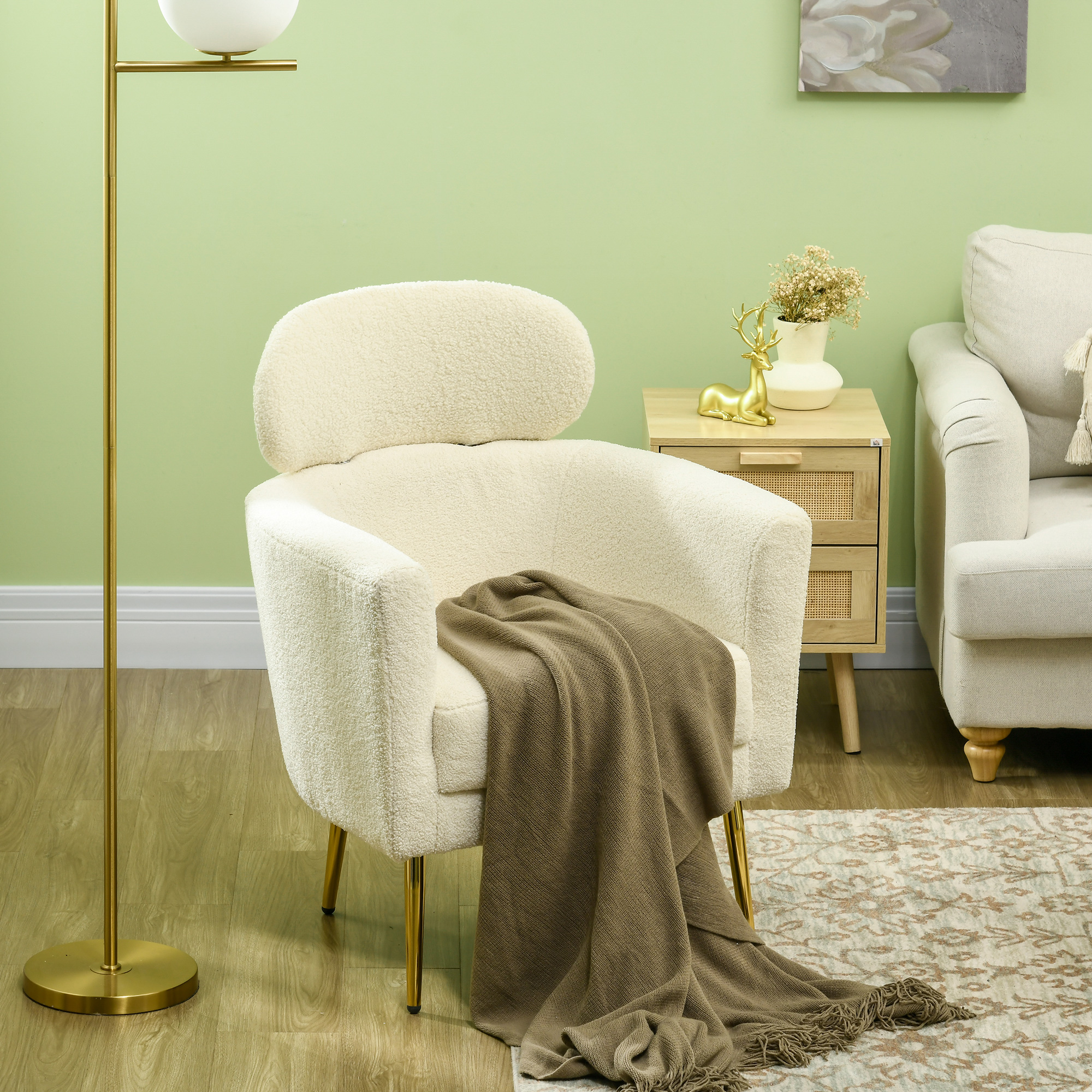 Silla de buclé color crema con patas doradas y un plaid marrón sobre un piso de madera.