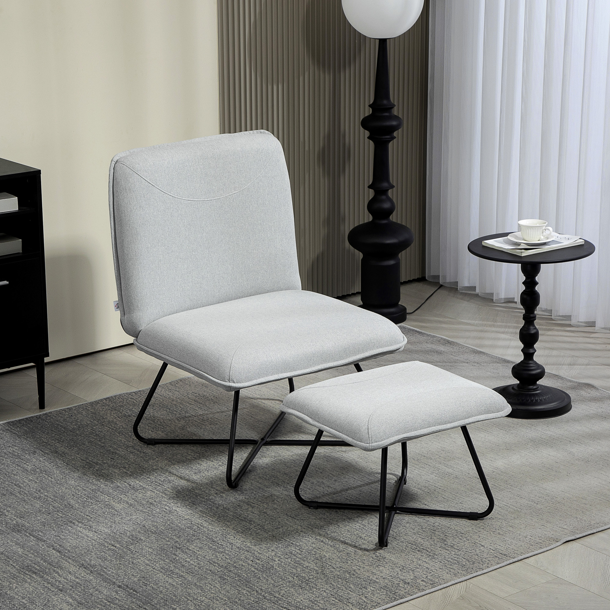 Silla y otomana grises con estructura de metal negro sobre una alfombra gris, junto a una lámpara negra y una mesa auxiliar.