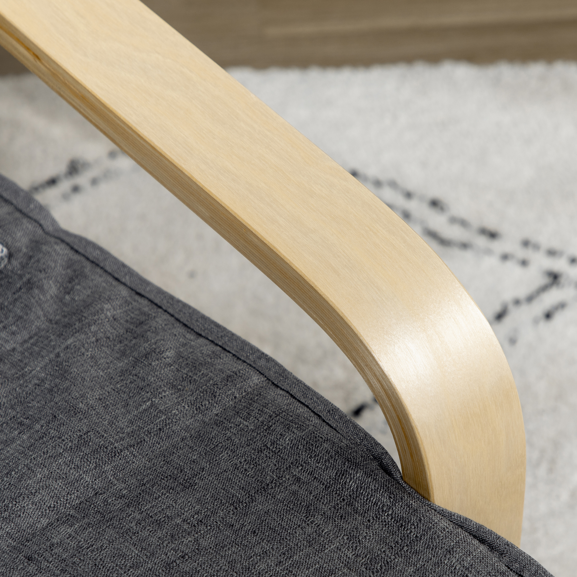 Un primer plano muestra un reposabrazos de madera unido a una silla de tela gris, con una alfombra estampada al fondo.