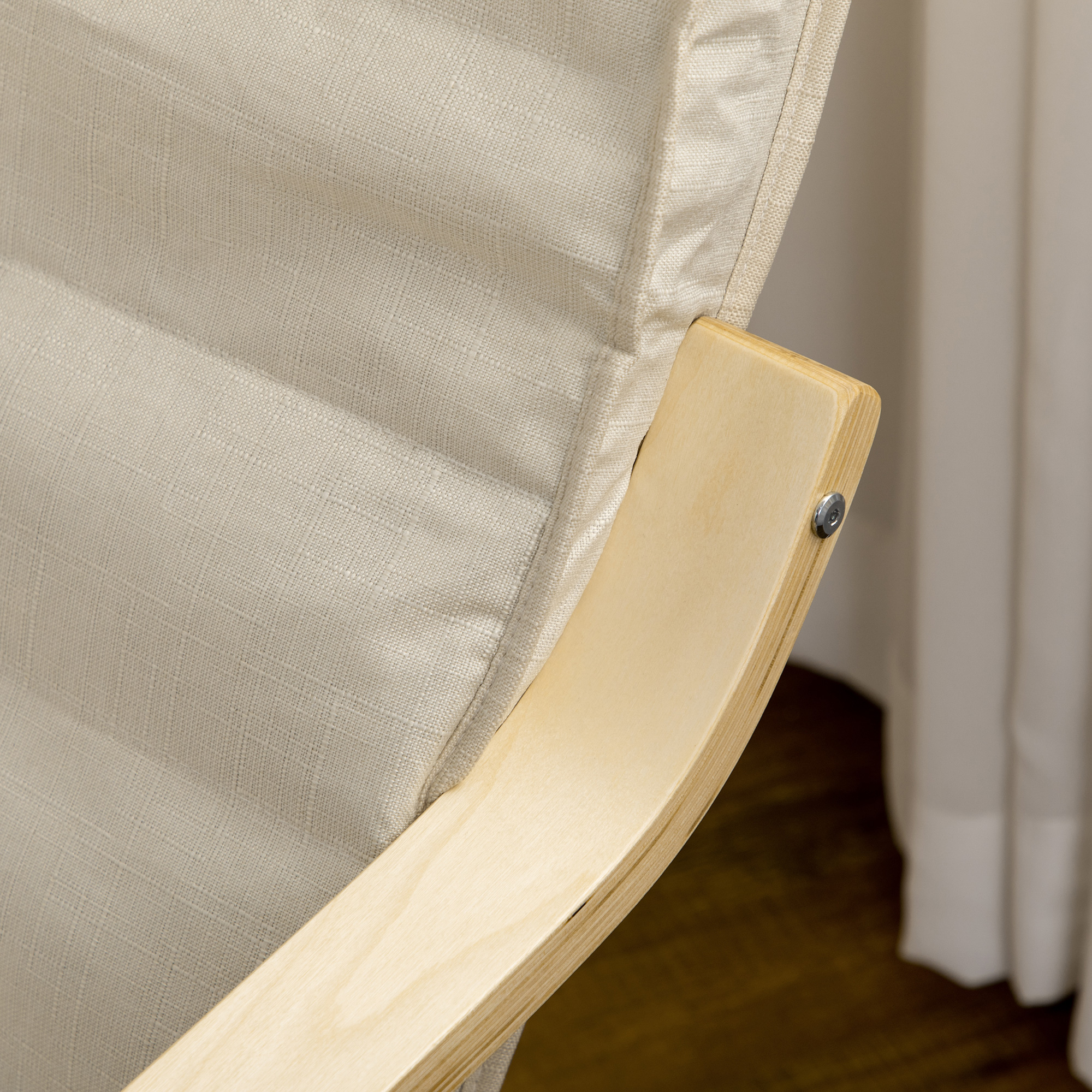 Un primer plano muestra el brazo de una silla de cojín beige, destacando el marco de madera y la textura de la tela.