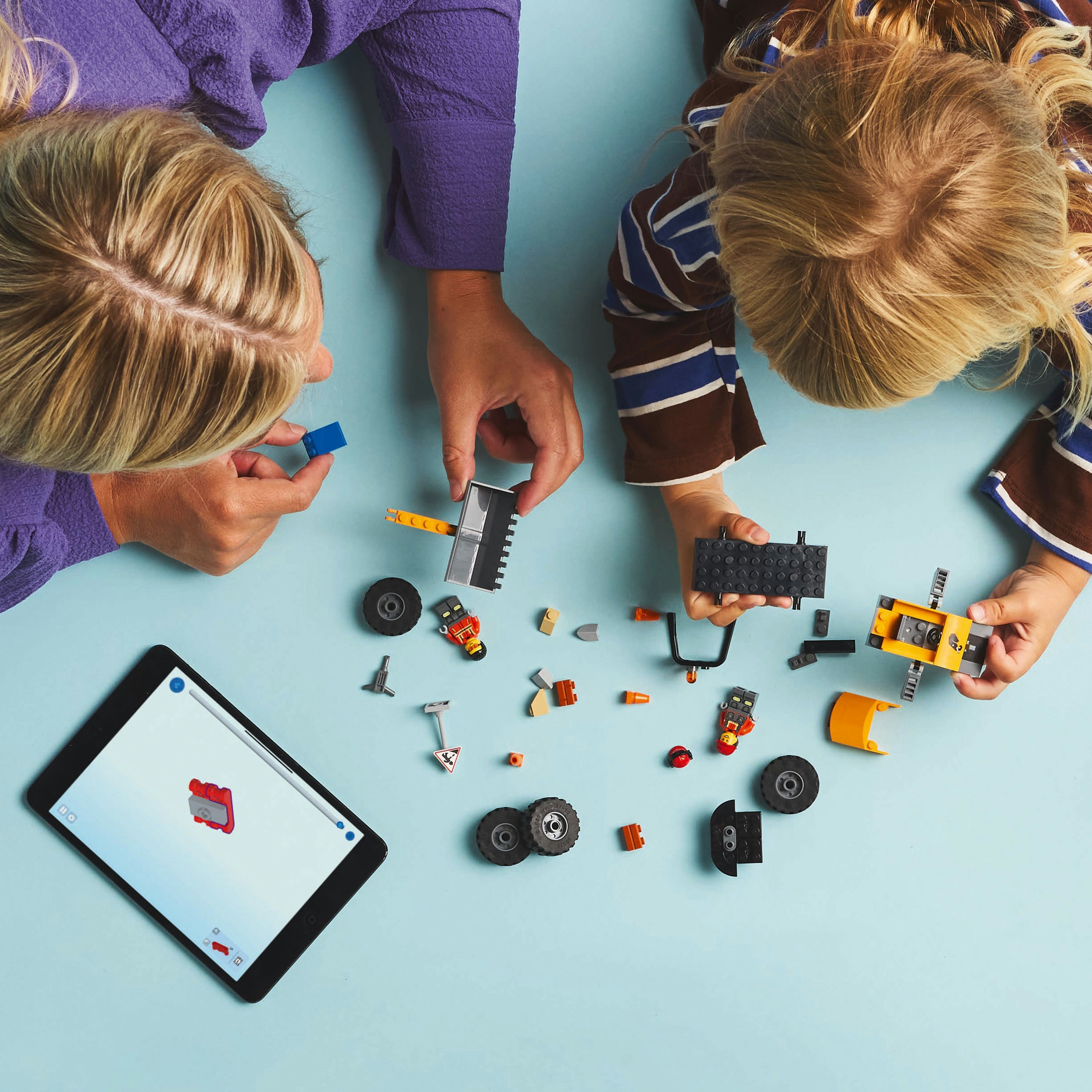 Talimatları gösteren bir tabletle bir LEGO City inşaat setini bir araya getiren bir çocuk ve yetişkinin yukarıdan çekilmiş fotoğrafı.