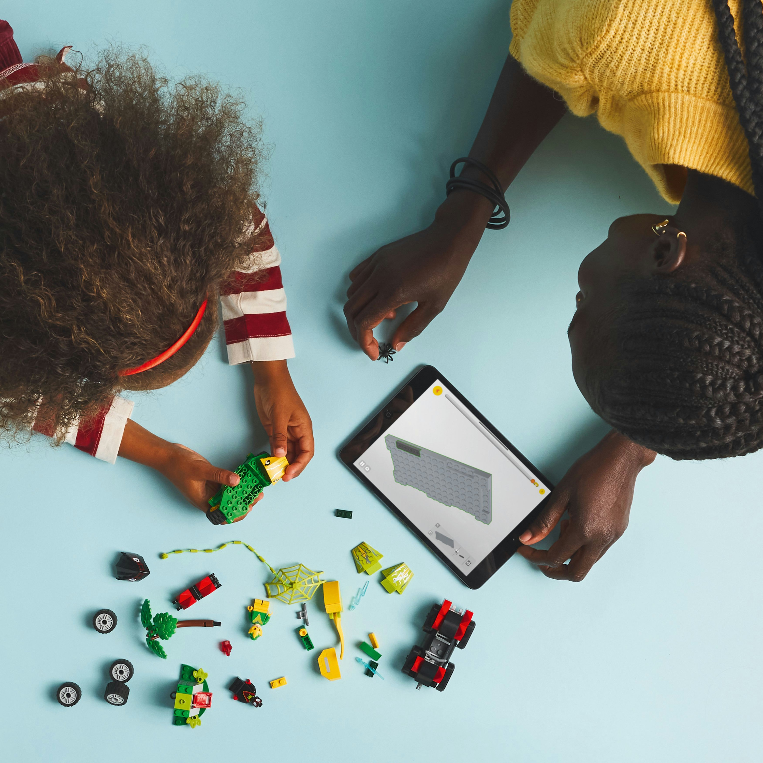 Dwie osoby budują zestaw Lego Spider-Man: zielony pojazd, pajęczyna i czarny pojazd.