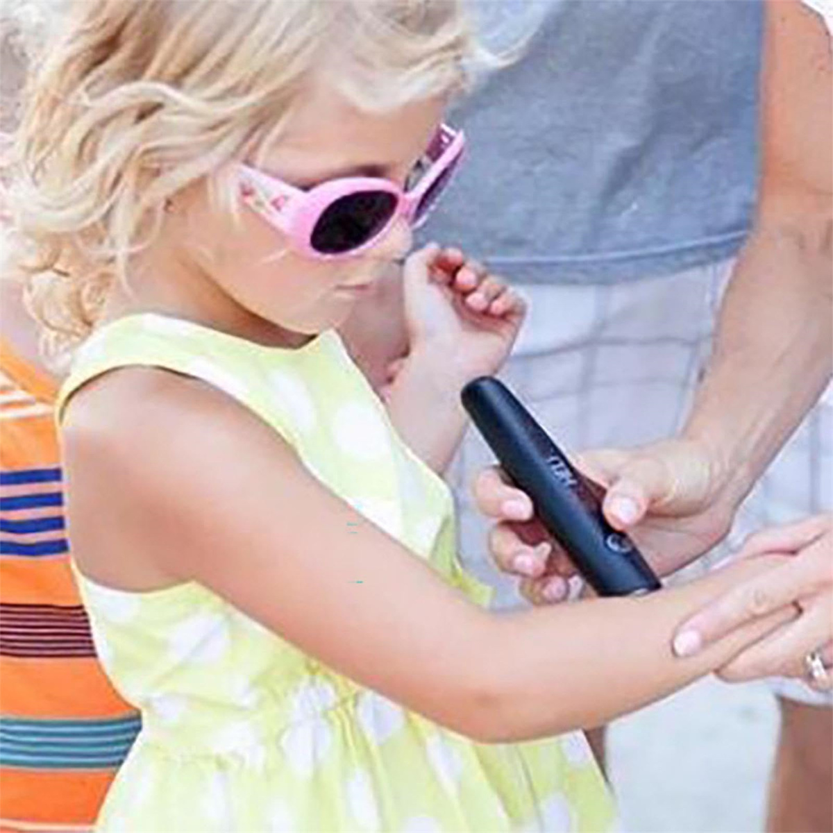 Mädchen in gelbem Kleid mit Sonnenbrille, Arm wird mit einem schwarzen Bite Helper-Gerät behandelt.