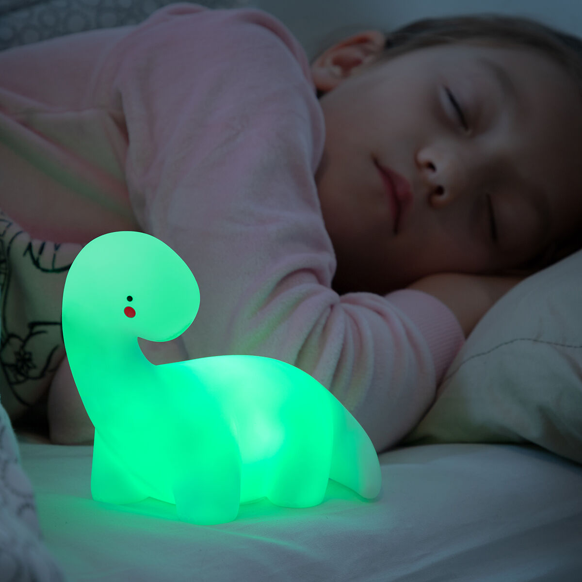 Un bambino che dorme accanto a una luce notturna a dinosauro verde brillante, su una superficie bianca.