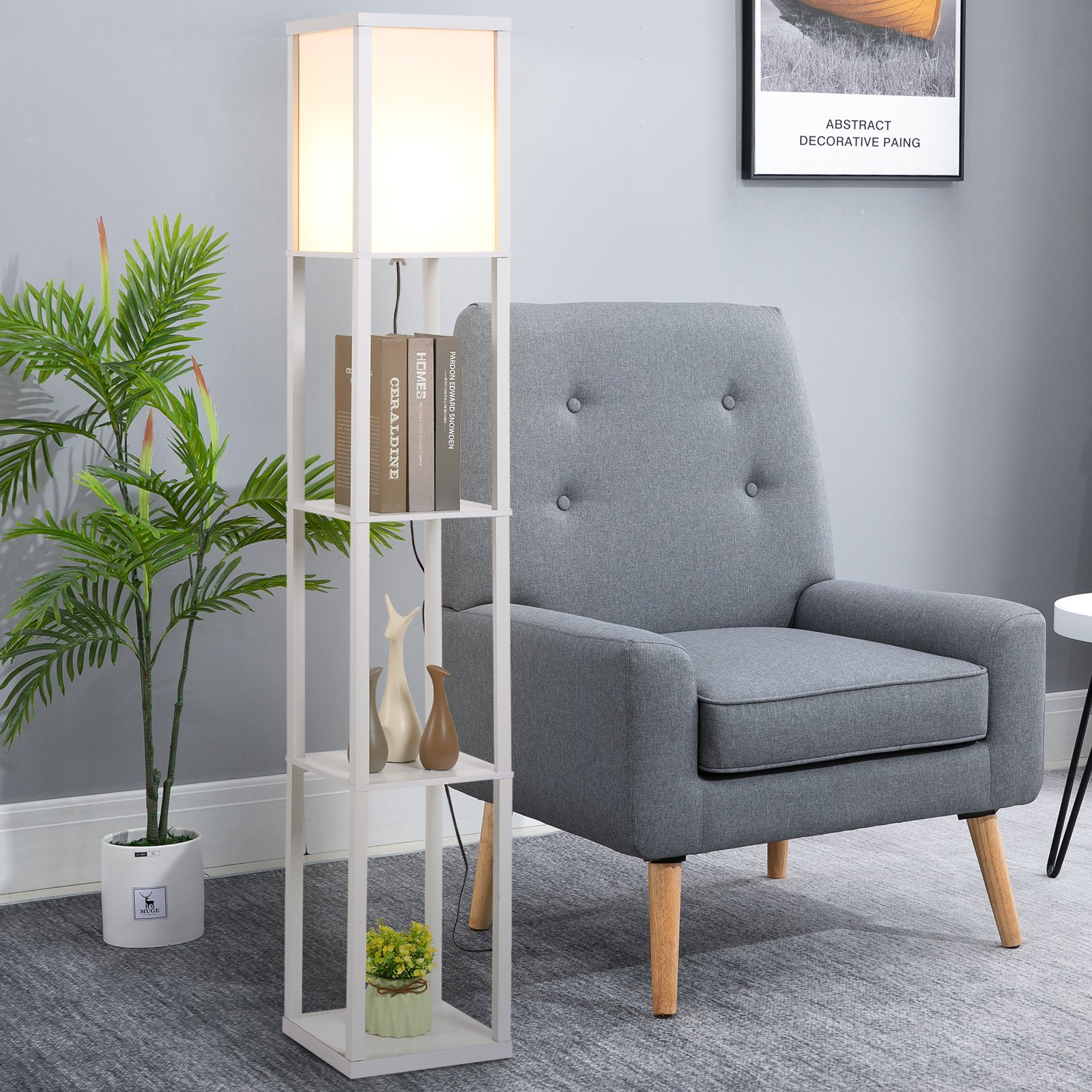Una lámpara de pie blanca con estantes, libros y objetos decorativos, junto a un sillón gris.