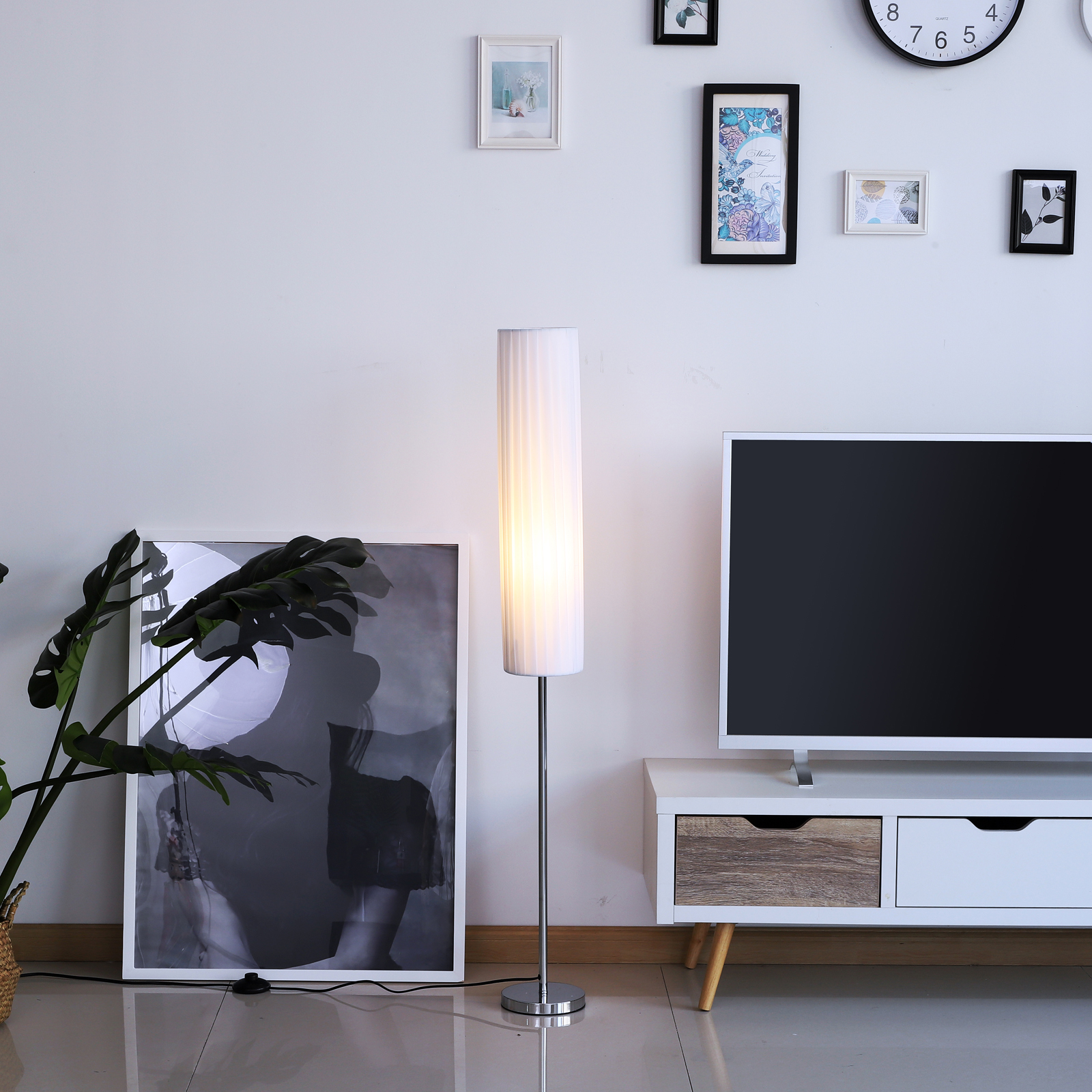 Una habitación con una lámpara de pie moderna. Un televisor y obras de arte están en la pared. Una planta en el suelo.
