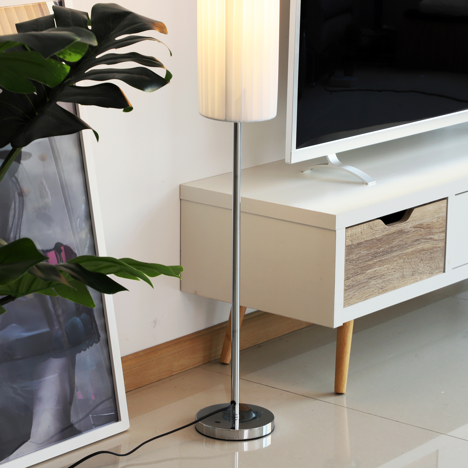 Una habitación con una lámpara de pie moderna. Un televisor y obras de arte están en la pared. Una planta en el suelo.