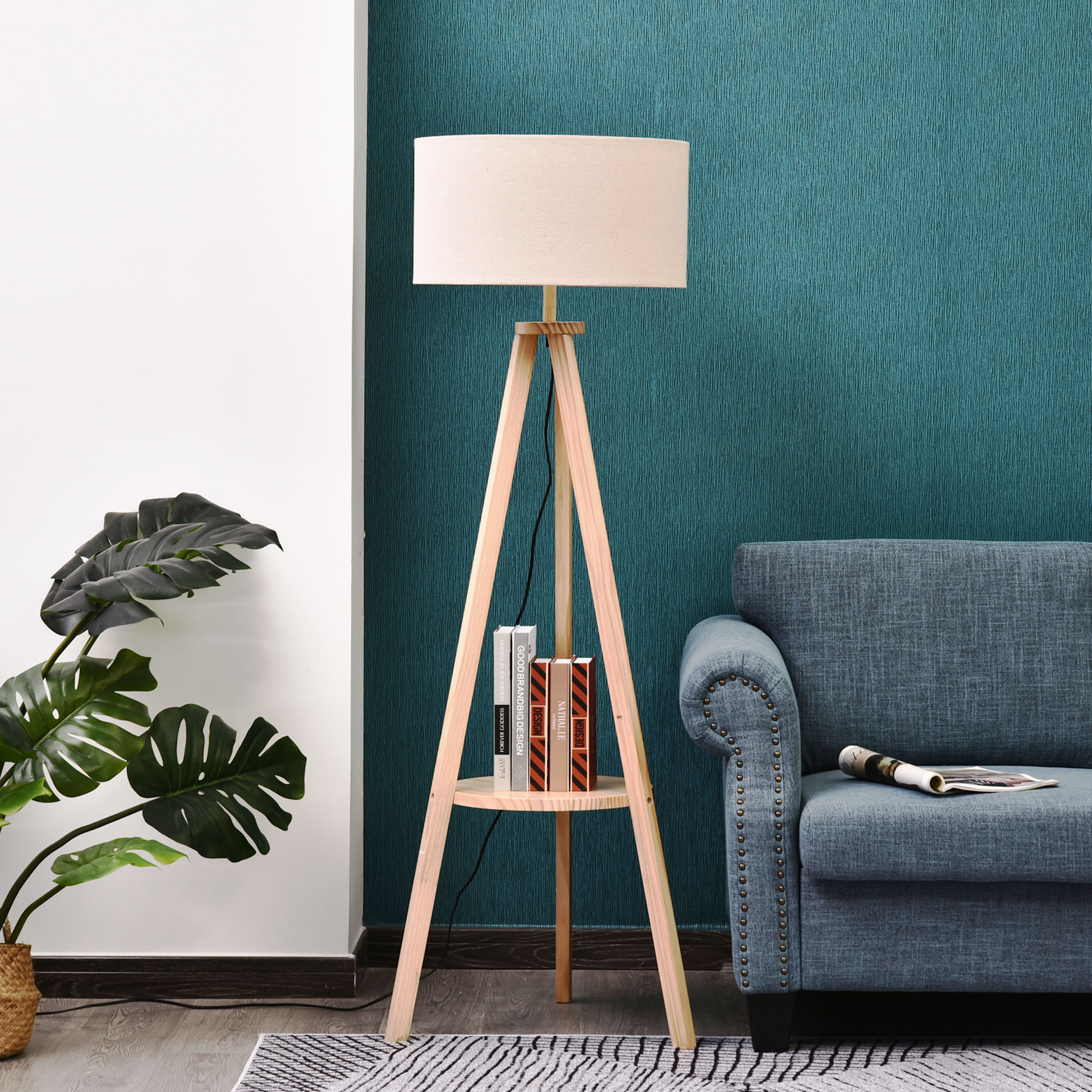 Lámpara de pie trípode de madera con pantalla beige y estante con libros, junto a sofá azul.