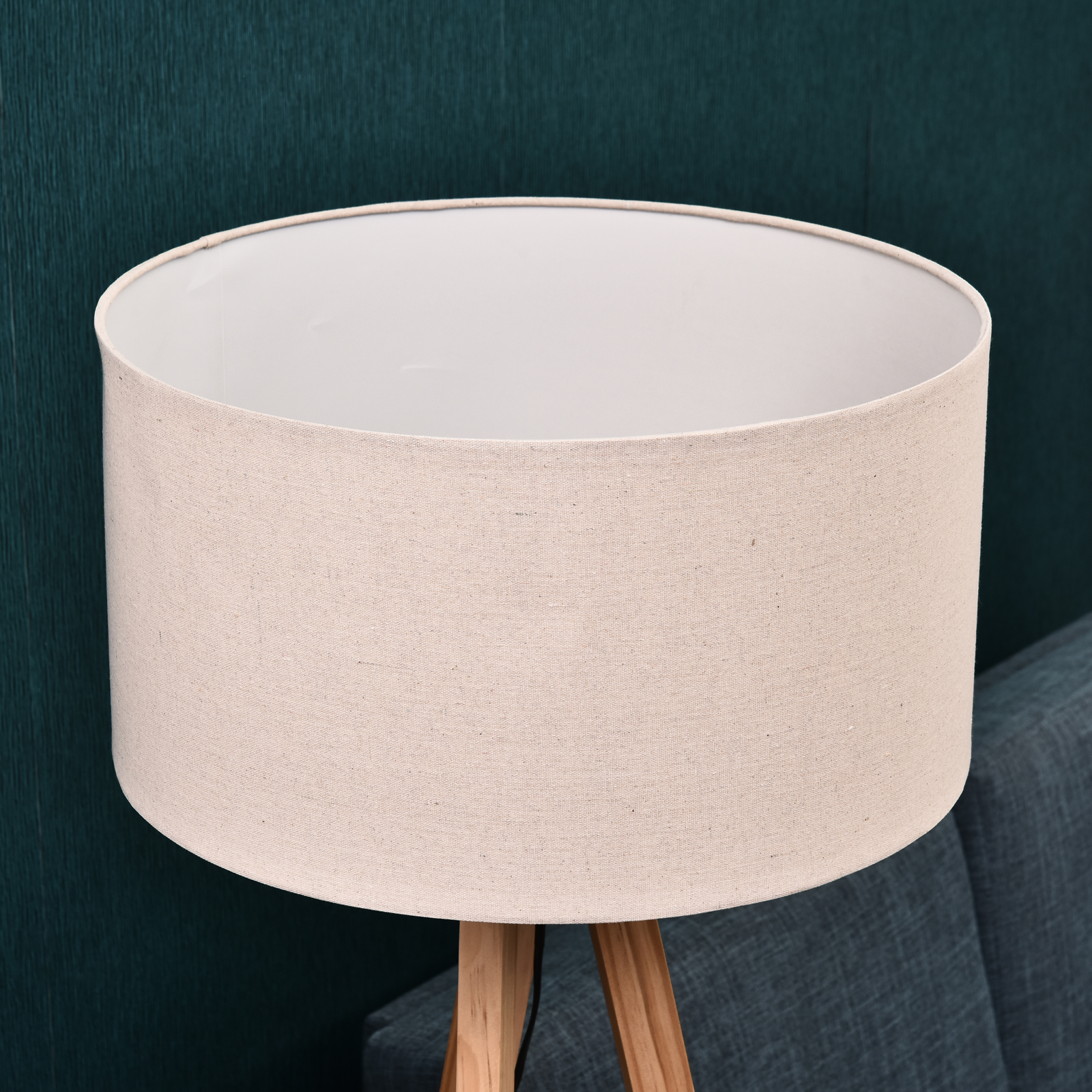 Primer plano de la pantalla beige de una lámpara de pie trípode de madera, mostrando su textura y forma.