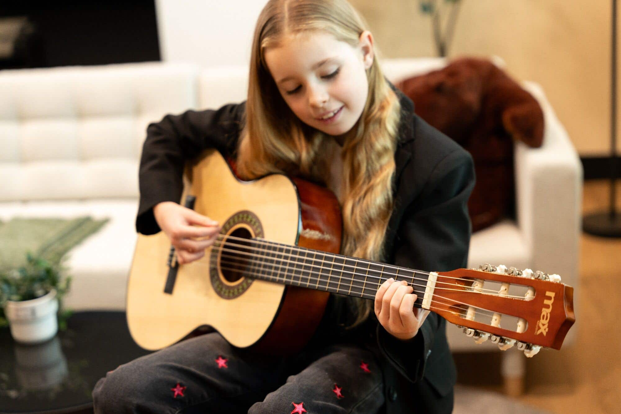 Een jong meisje speelt gitaar op een bank. Een teddybeer staat op de achtergrond.