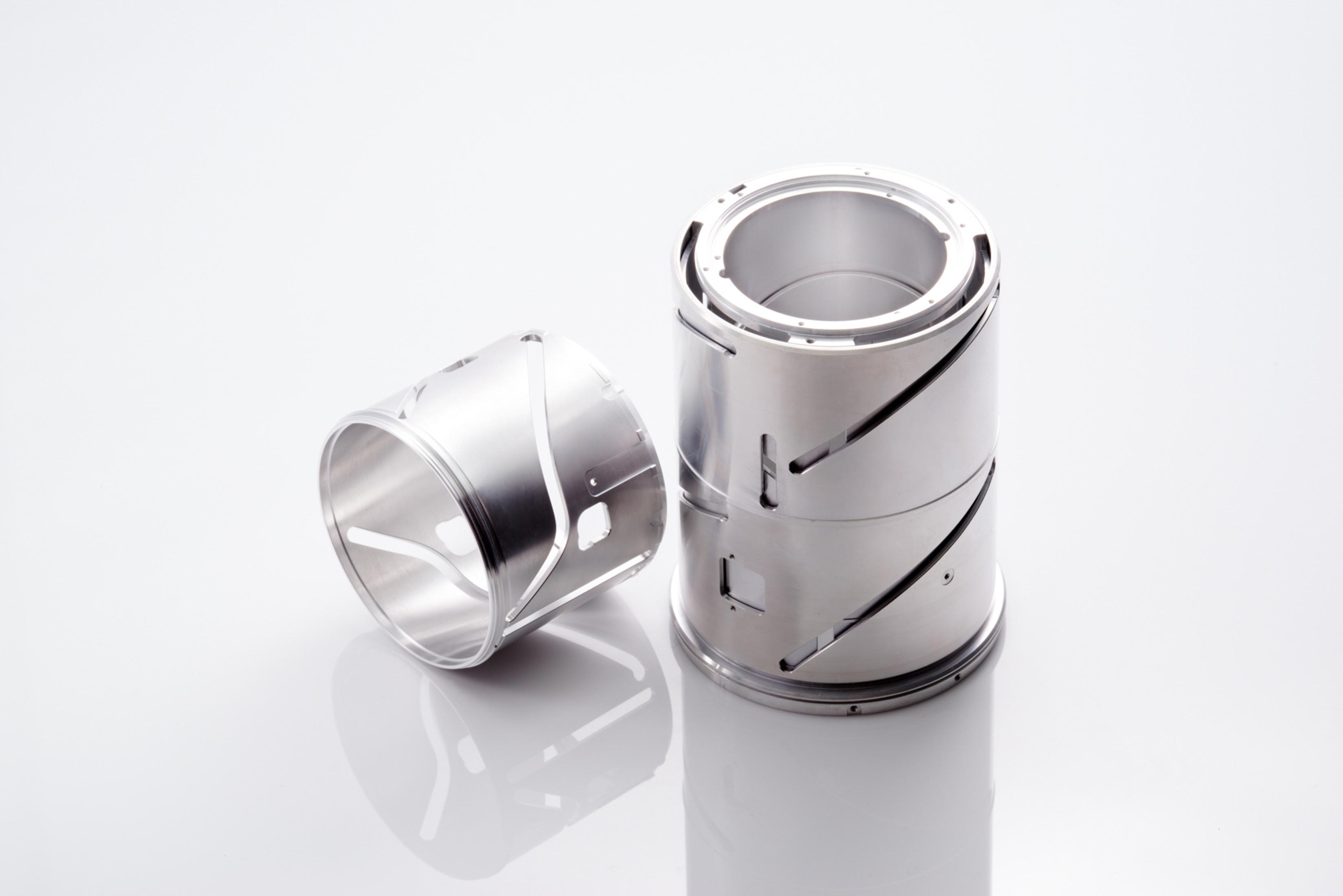 Zwei zylindrische Metallteile. Eines steht, das andere liegt. Beide haben Ausschnittsdesigns.
