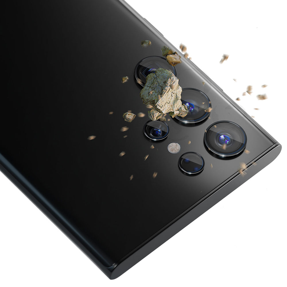 Na zdjęciu widoczny jest aparat telefoniczny z osłonami na obiektyw, na który spadają małe kamienie i gruz.