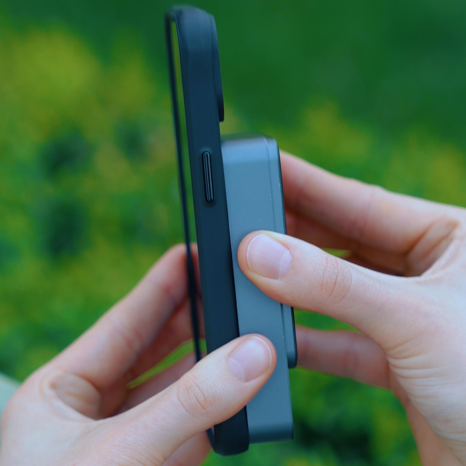 Ręce osoby trzymają czarne etui na telefon z szarym akcesorium do ładowania.