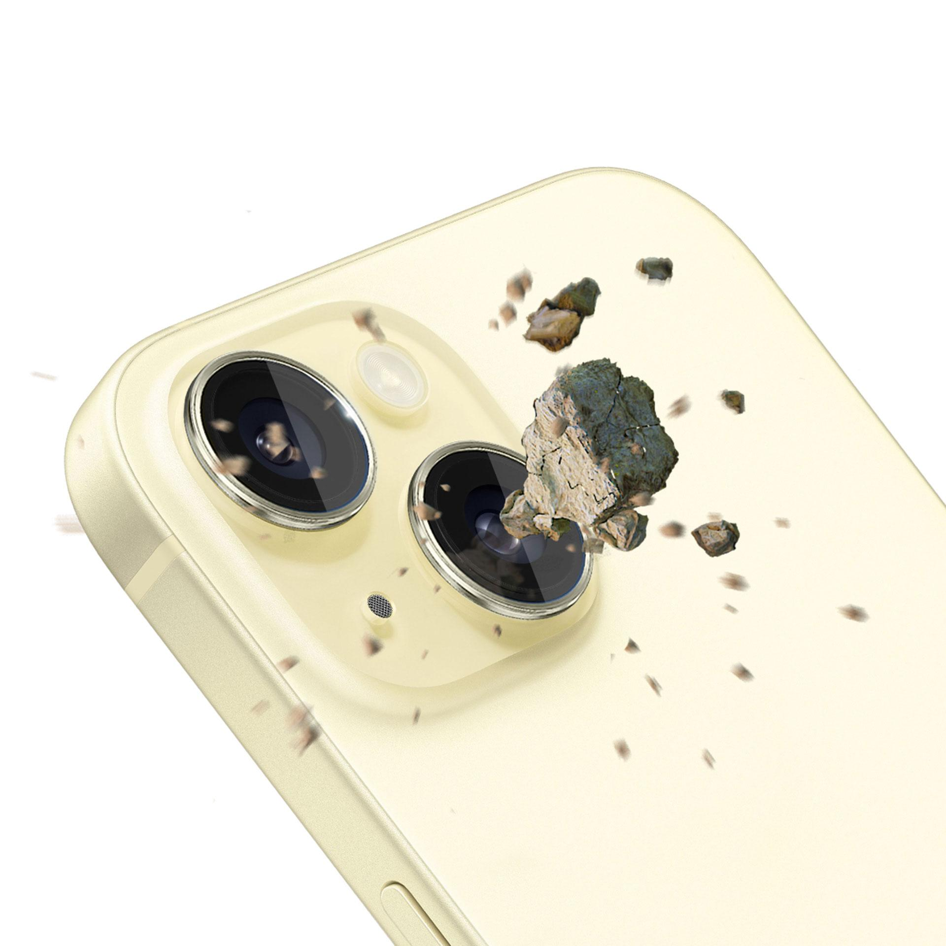 Un telefono giallo con protezioni per l'obiettivo della fotocamera viene colpito da piccole rocce. Lo sfondo è bianco.