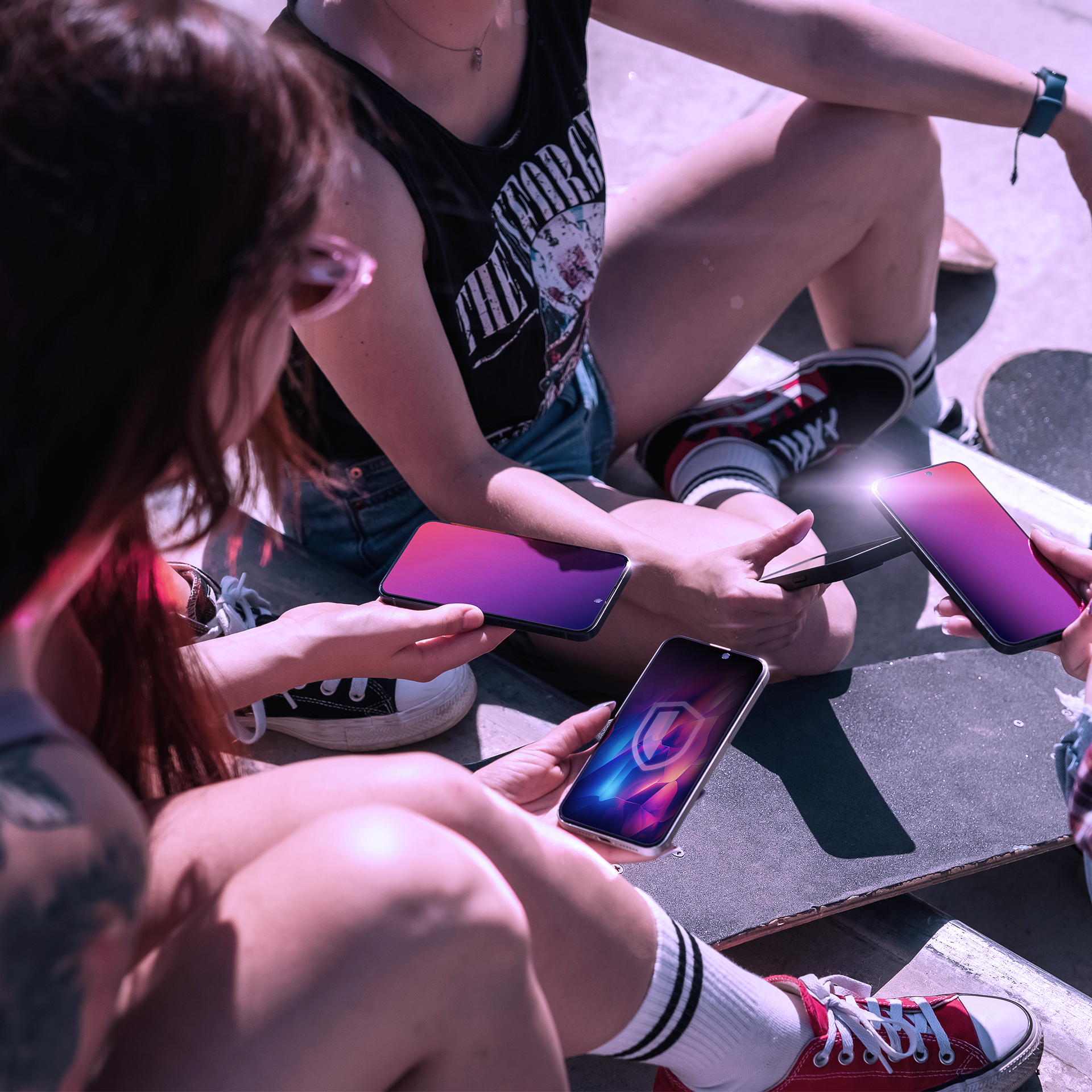 Tre persone su skateboard che tengono telefoni con schermi colorati. Sono seduti su una rampa.