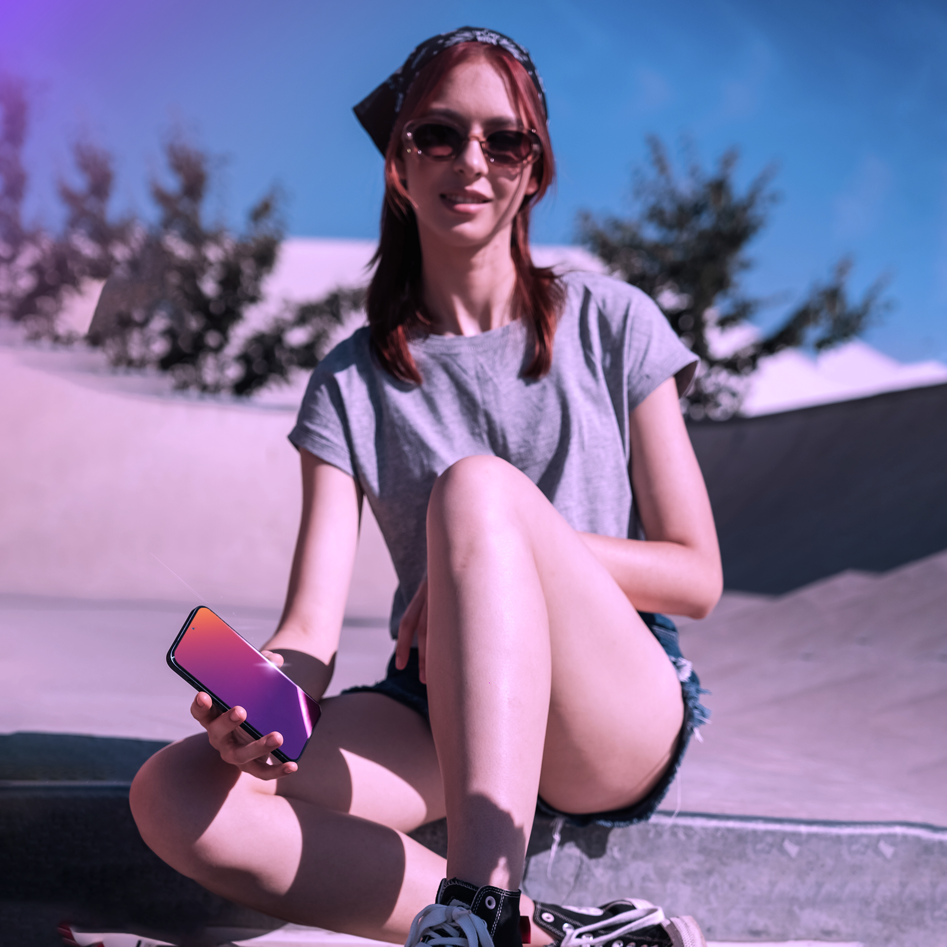 Una donna seduta su una rampa da skate, che tiene un telefono con un display vibrante.