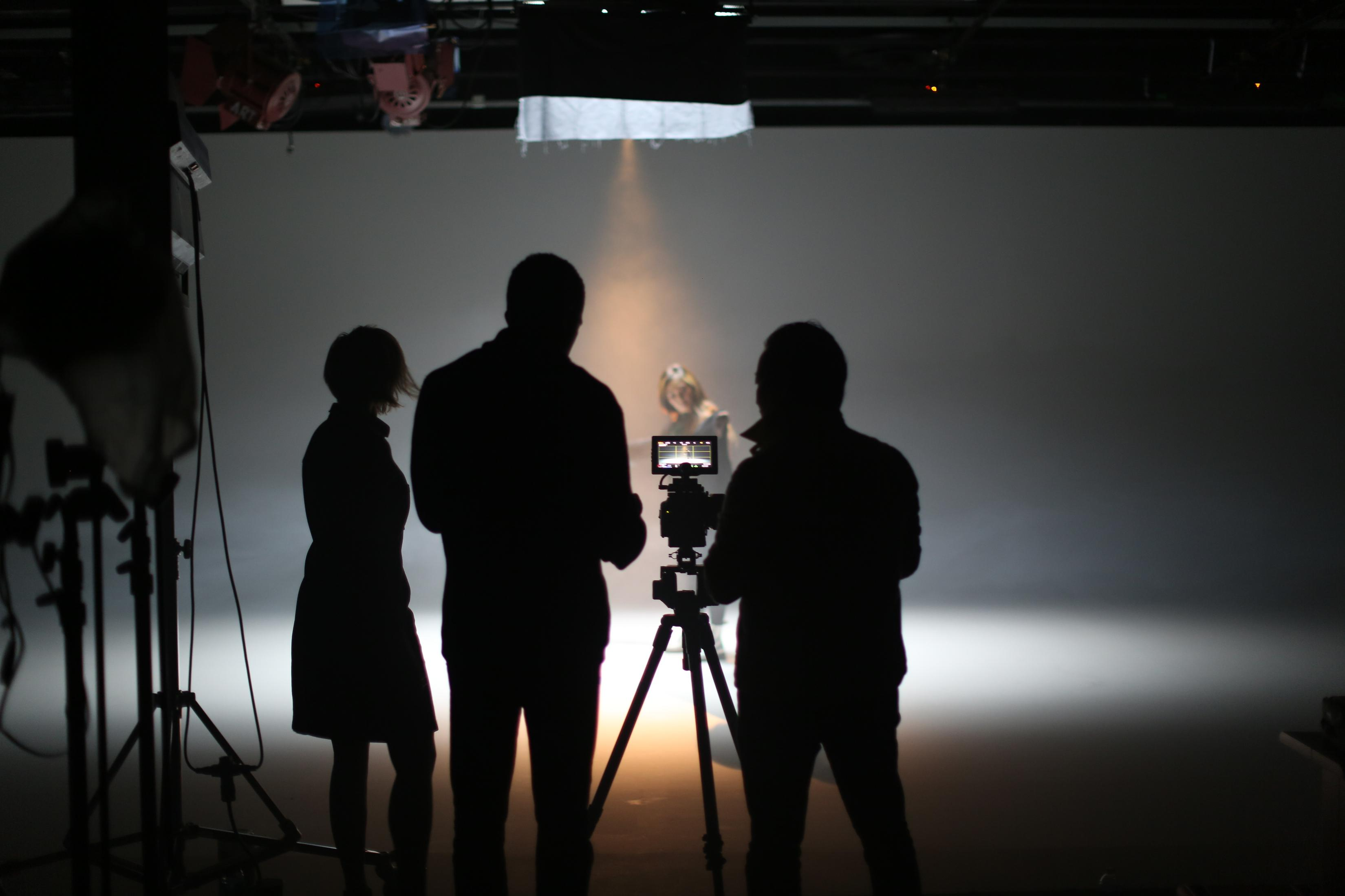 Un set cinematografico con silhouette di tre persone, una telecamera e attrezzature per l'illuminazione.