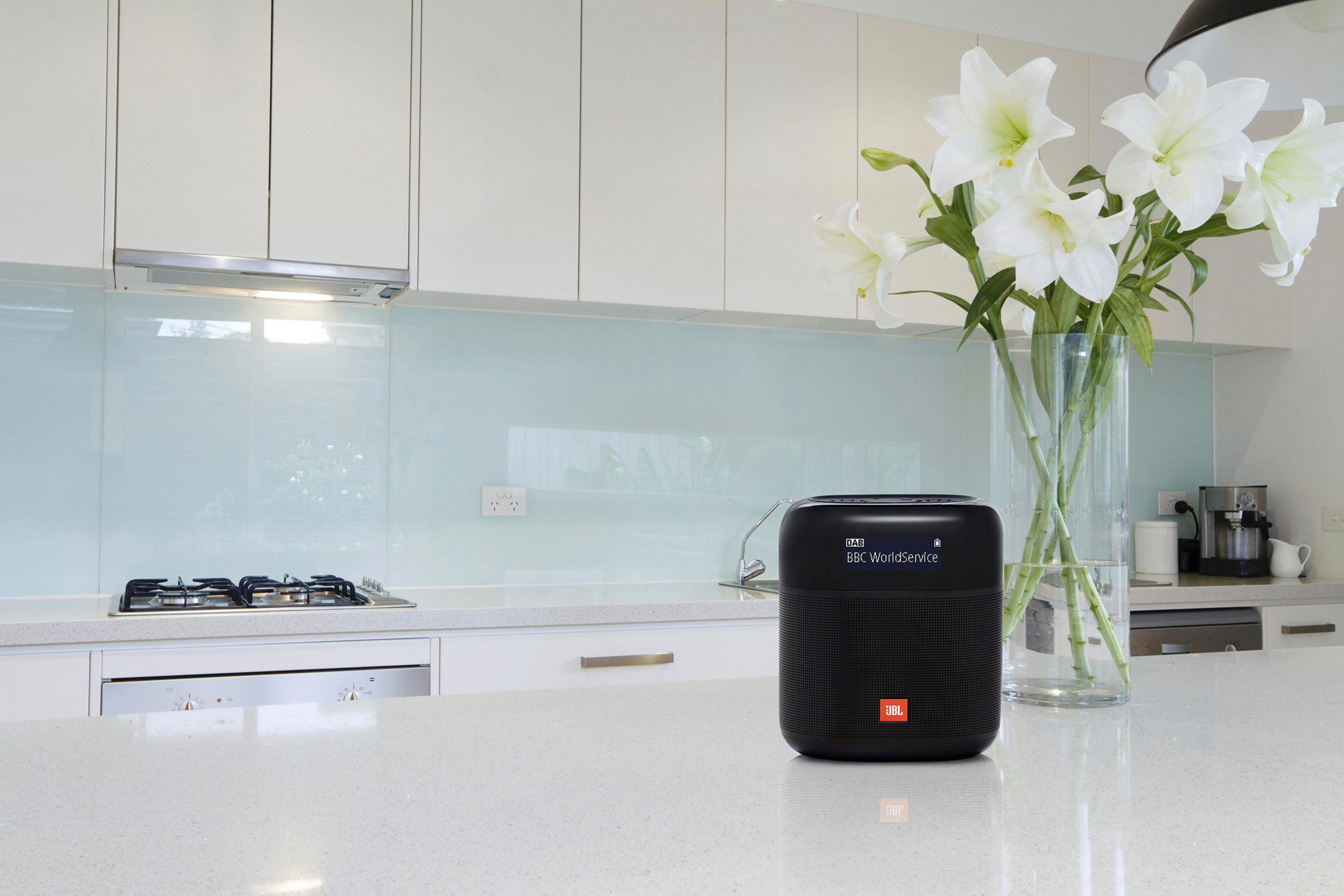 Un altoparlante JBL nero è su un bancone da cucina bianco con gigli bianchi in un vaso di vetro.