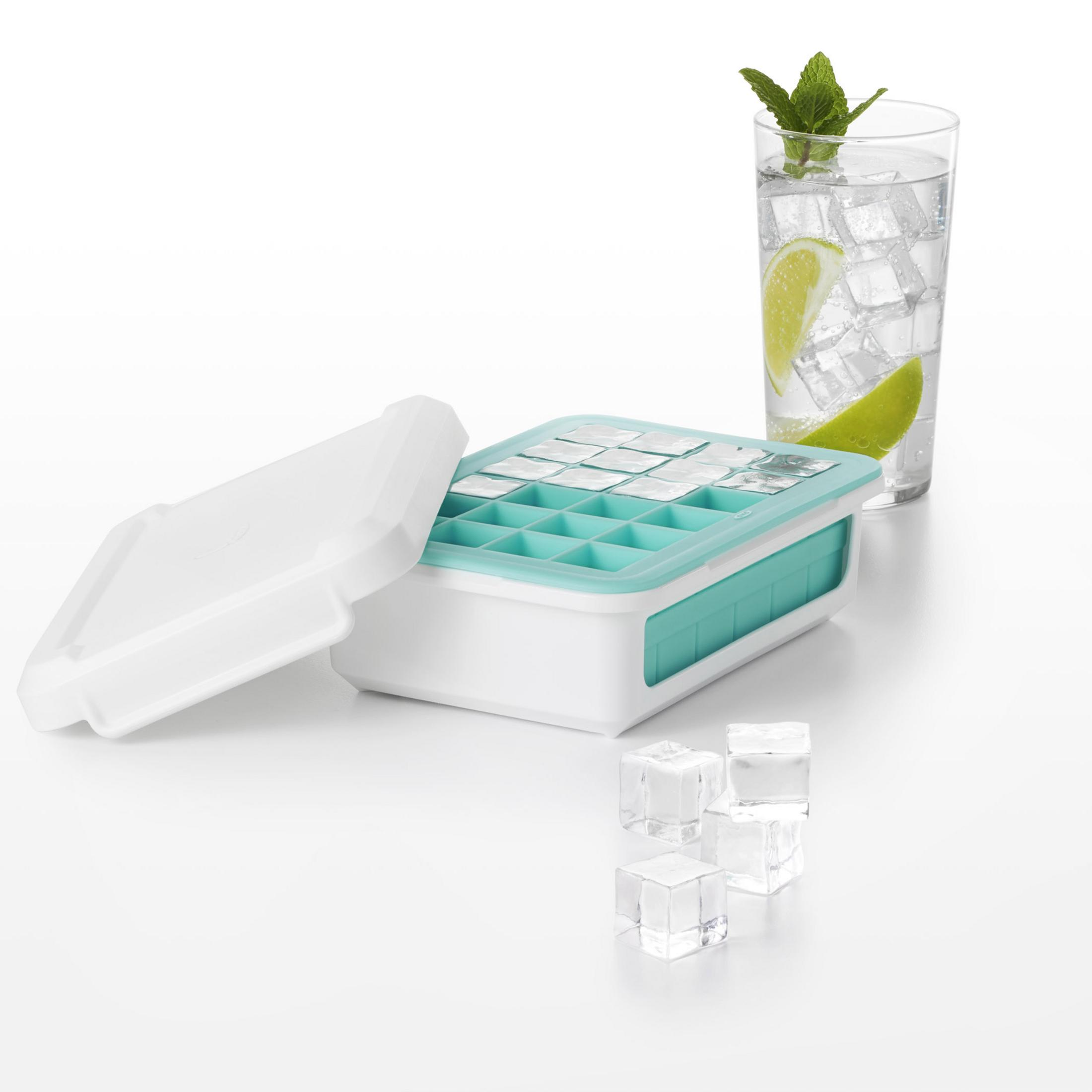 Eiswürfelform mit Würfeln, ein Glas Wasser mit Limette und Minze auf einer weißen Oberfläche.